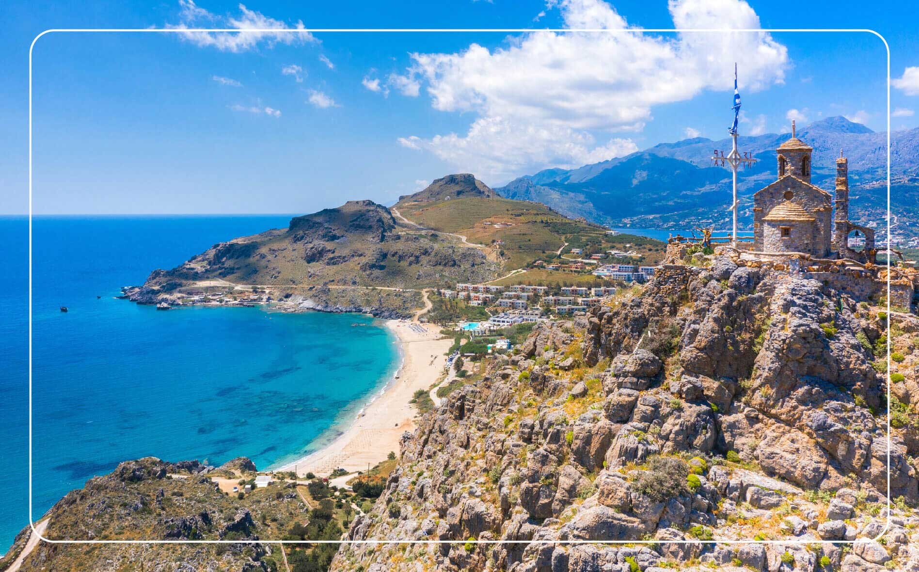 Aerial view of the Greek coastline with a church in the right foreground and rugged mountains rising in the background.