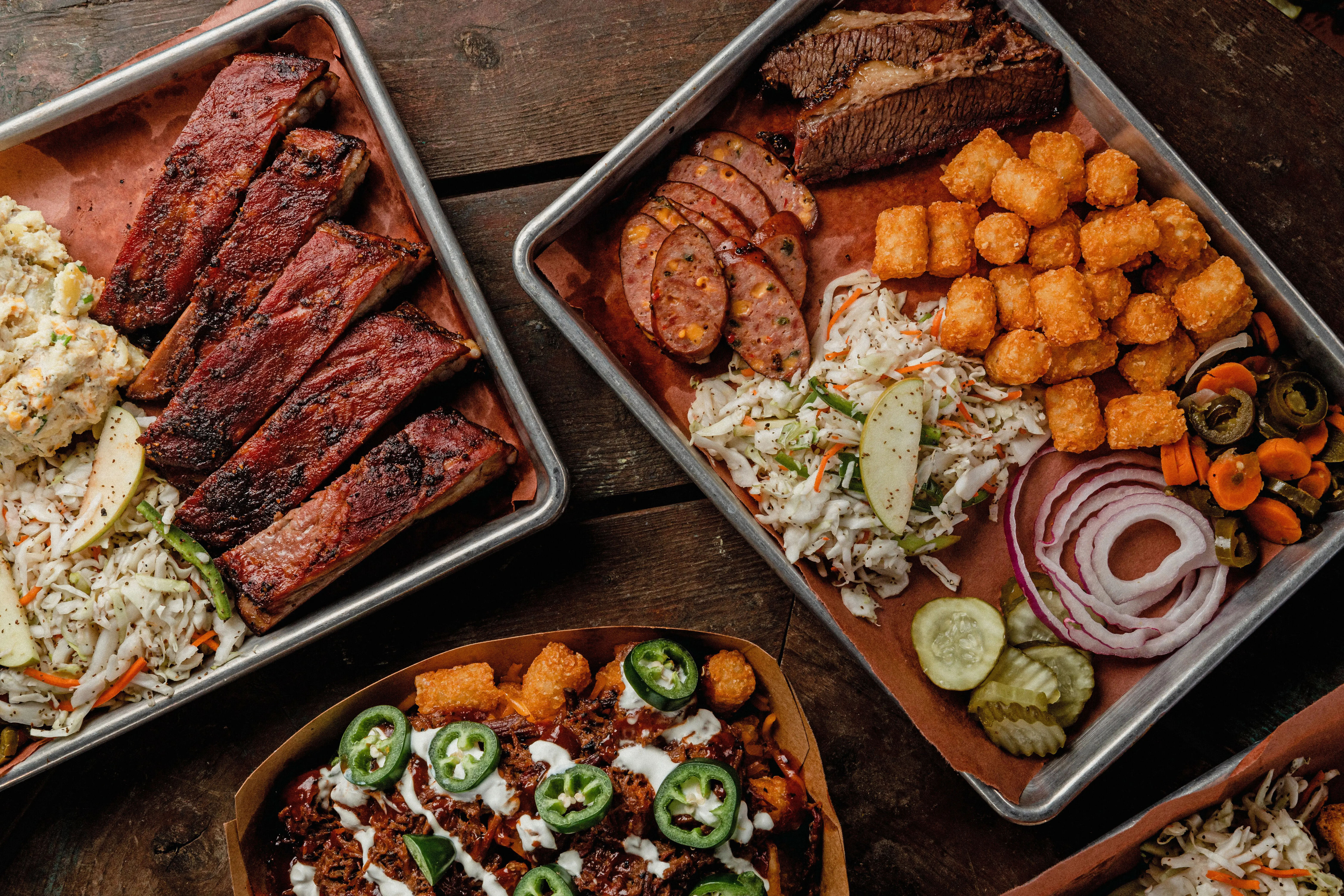Barbeque platters with brisket, ribs, smoked sausage, coleslaw, and tater tots