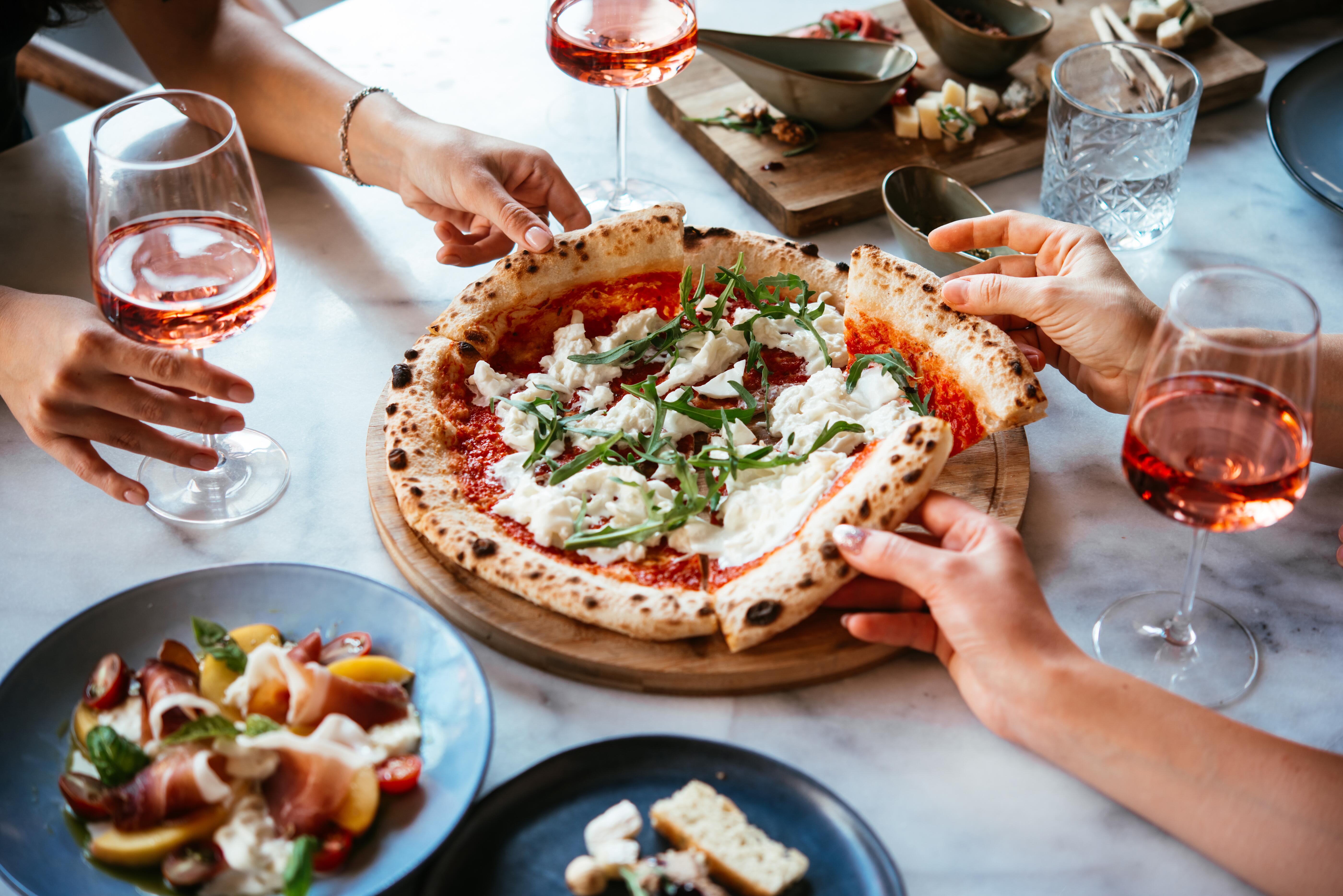 Friends enjoy a dinner party with pizza and rose wine in a bar or a restaurant