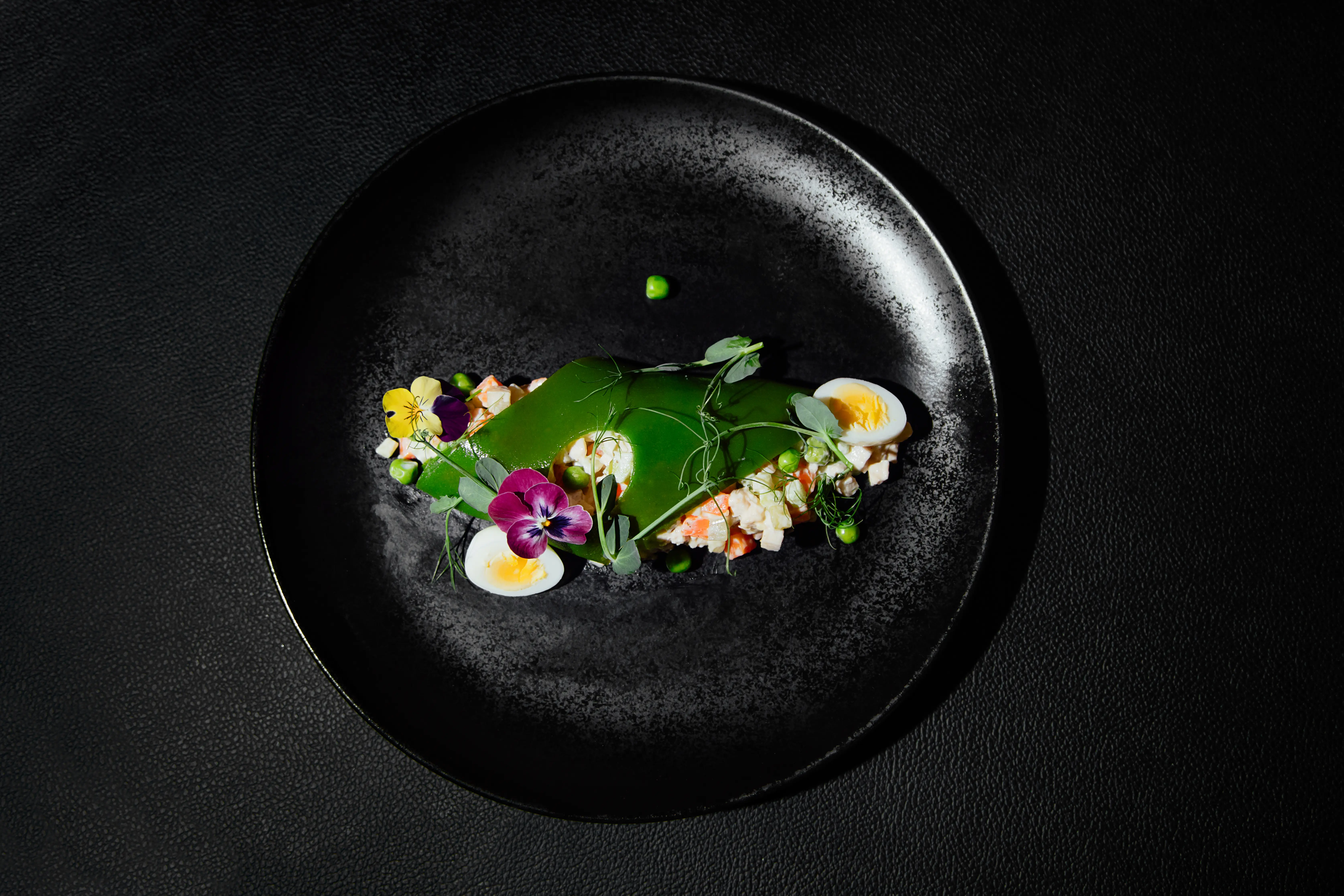 Image of a fancy salad served on a black plate.