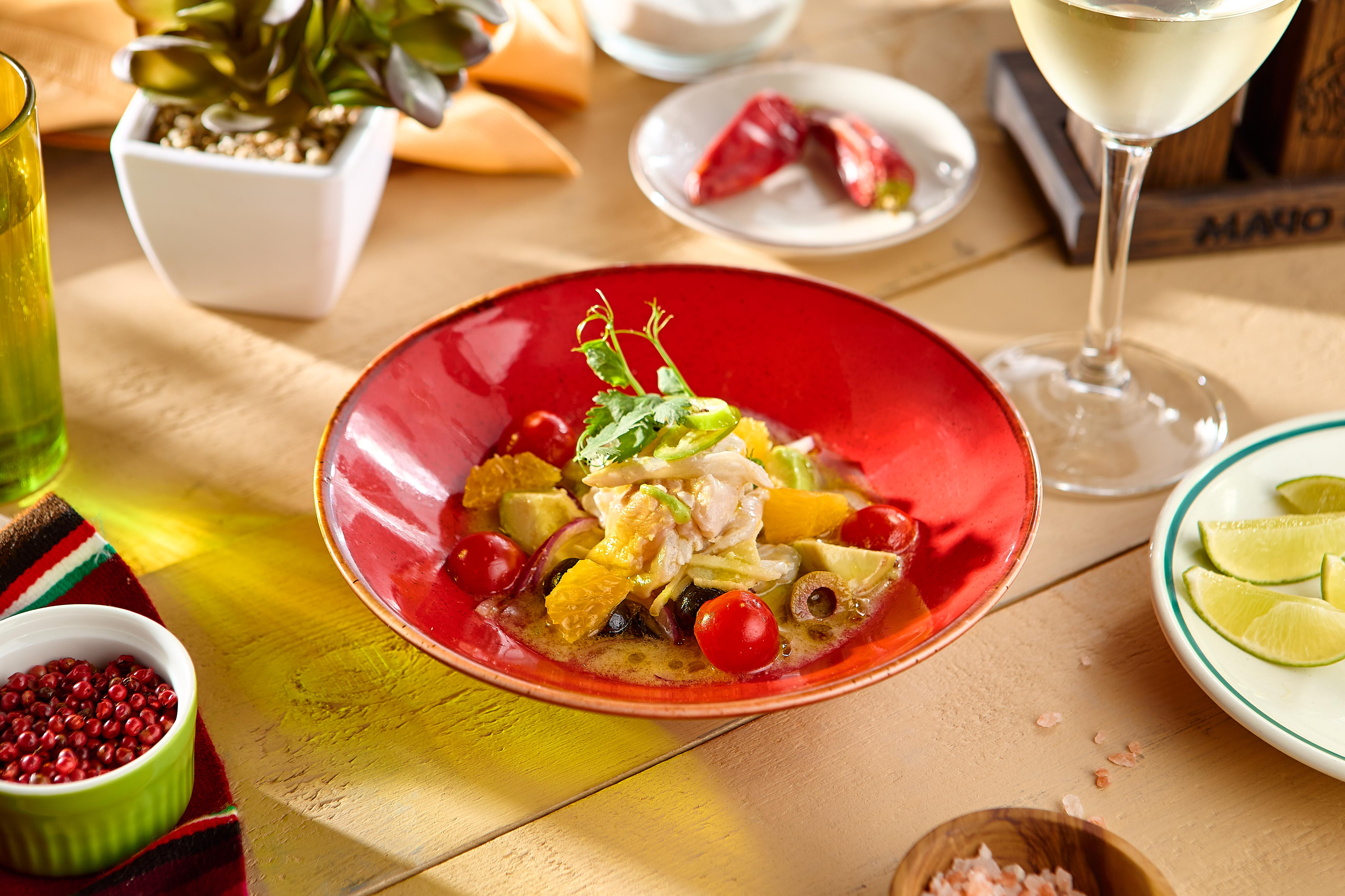 Fresh Fish Ceviche with Olives, Orange, Avocado, and Tomatoes on a Red Plate