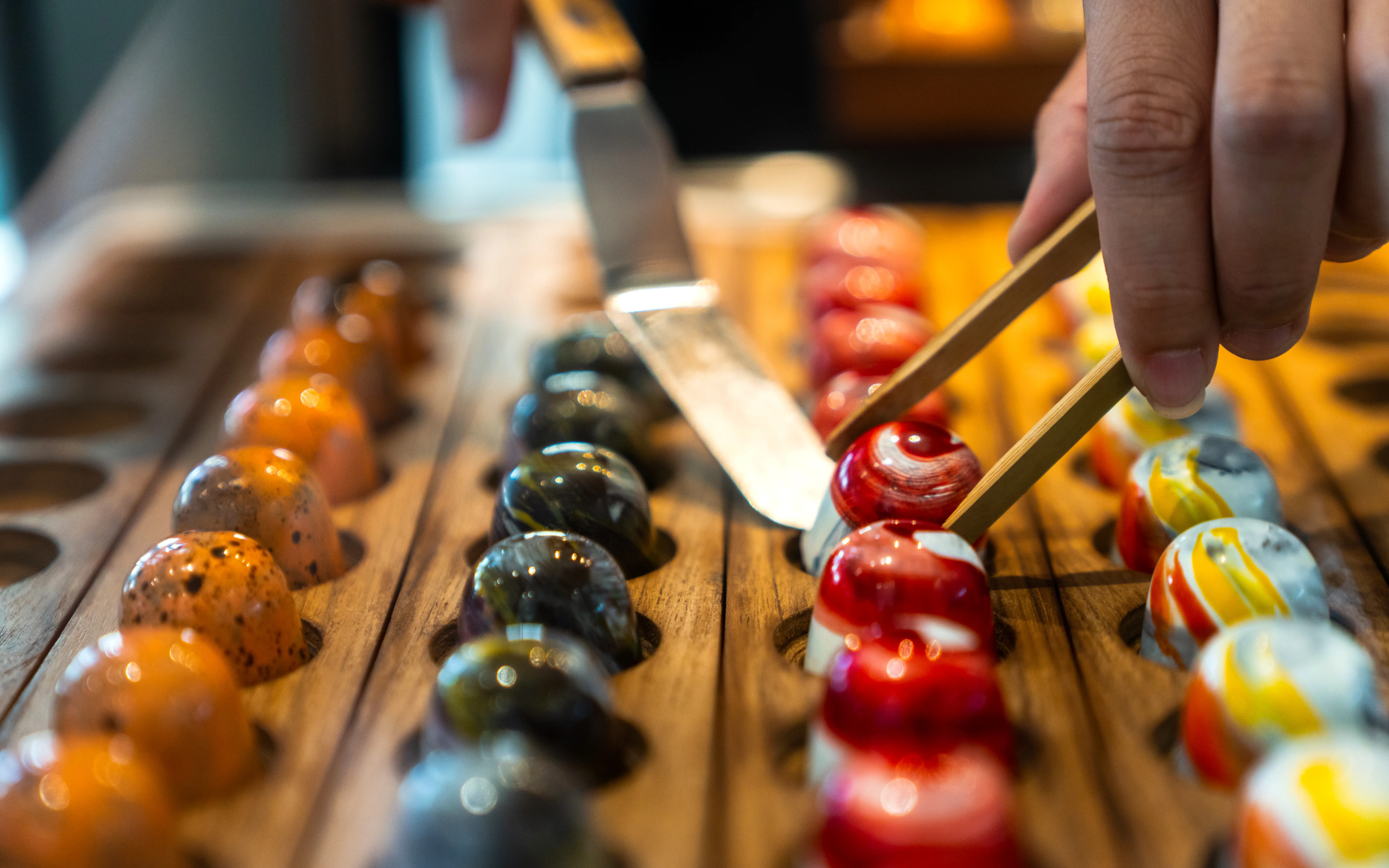 Chocolatier picking up a handcrafted confection from a row of shiny and colorful chocolate bonbons