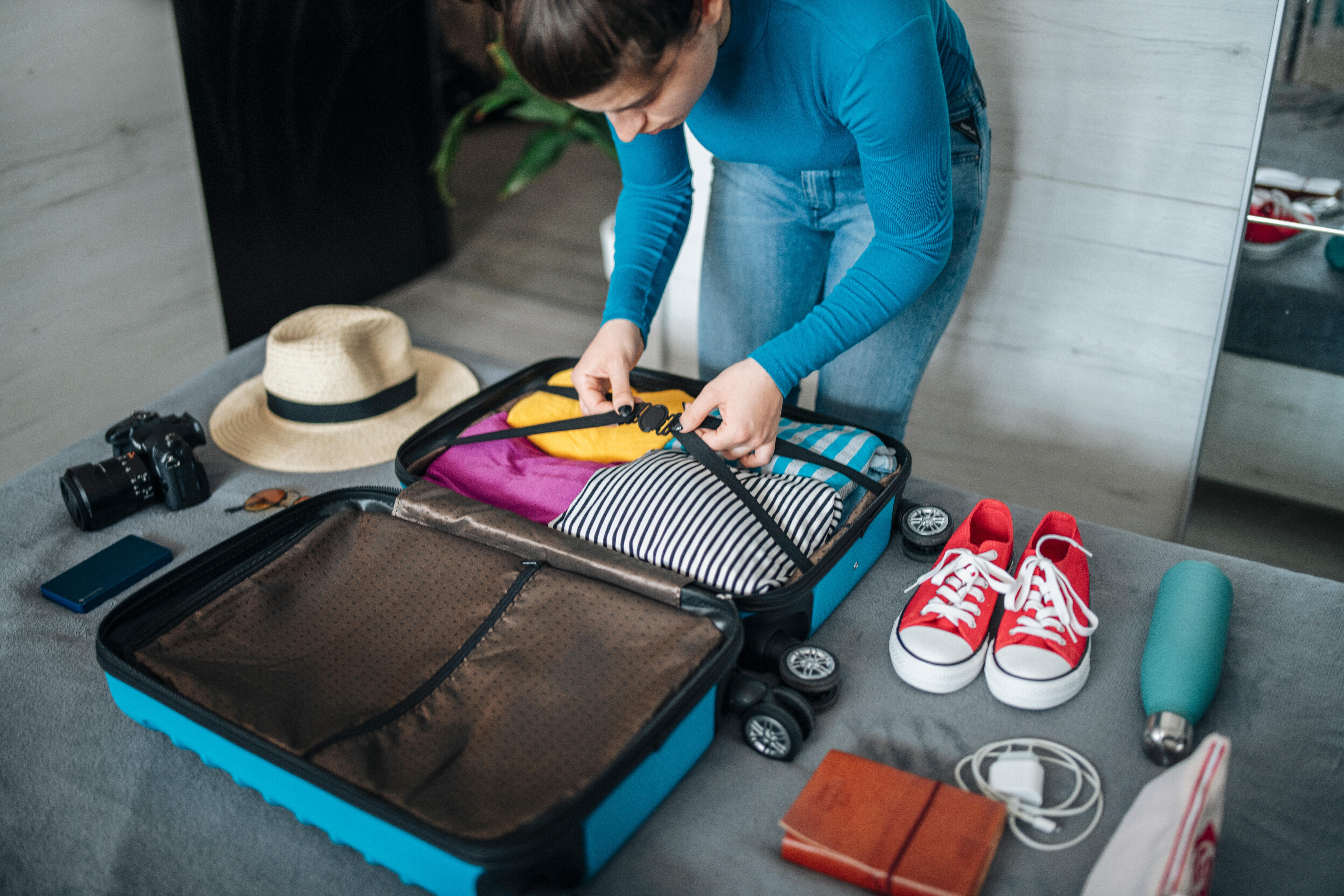 Woman neatly packing her suitcase ready for a vacation, clothes, camera, hat, sunglasses, sneakers, phone and charger.