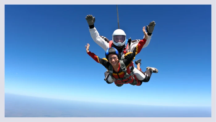 Two people are shown mid-air after jumping out of a plane for a skydiving experience. 