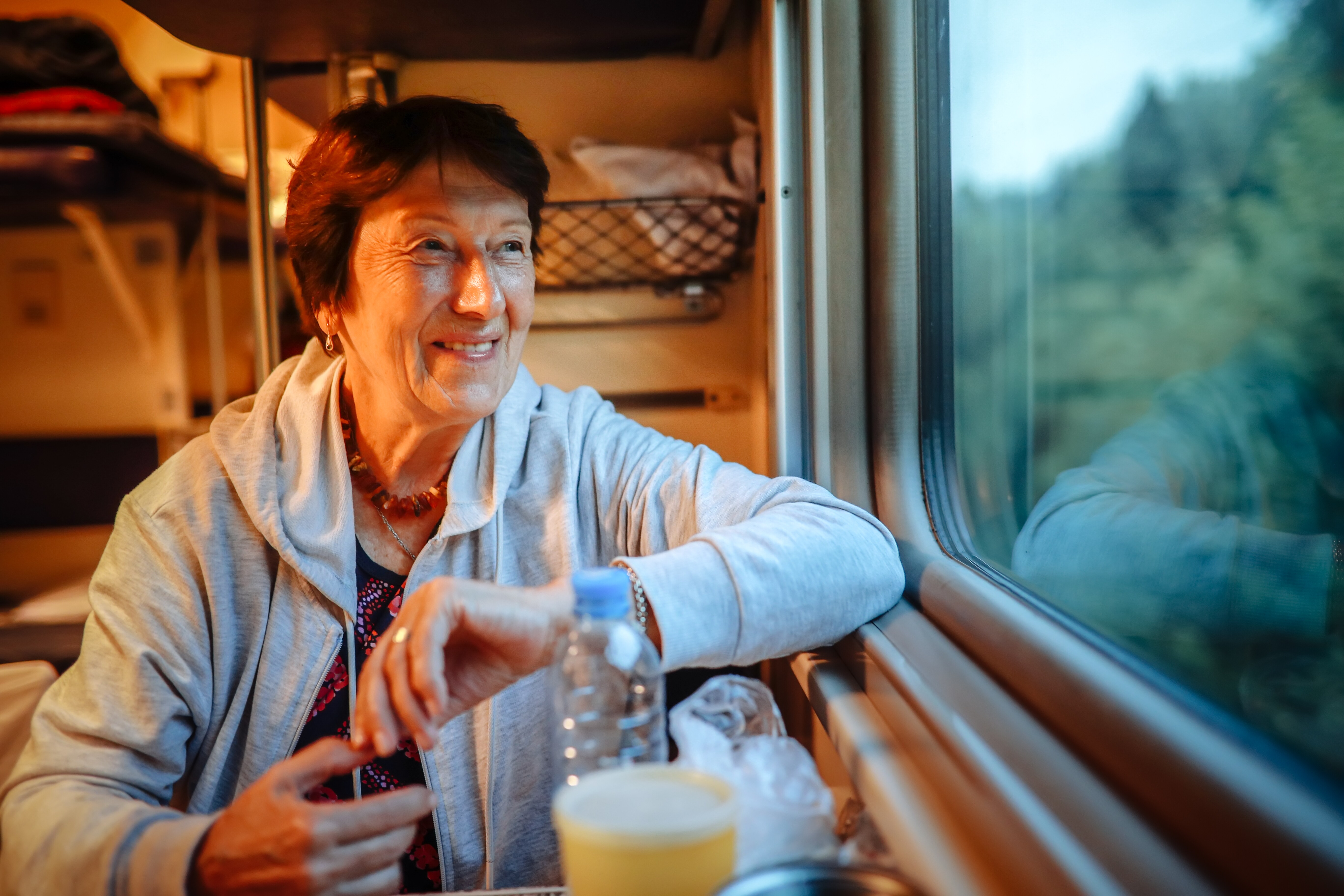 Image of an older woman smiling and looking out the window on a train.
