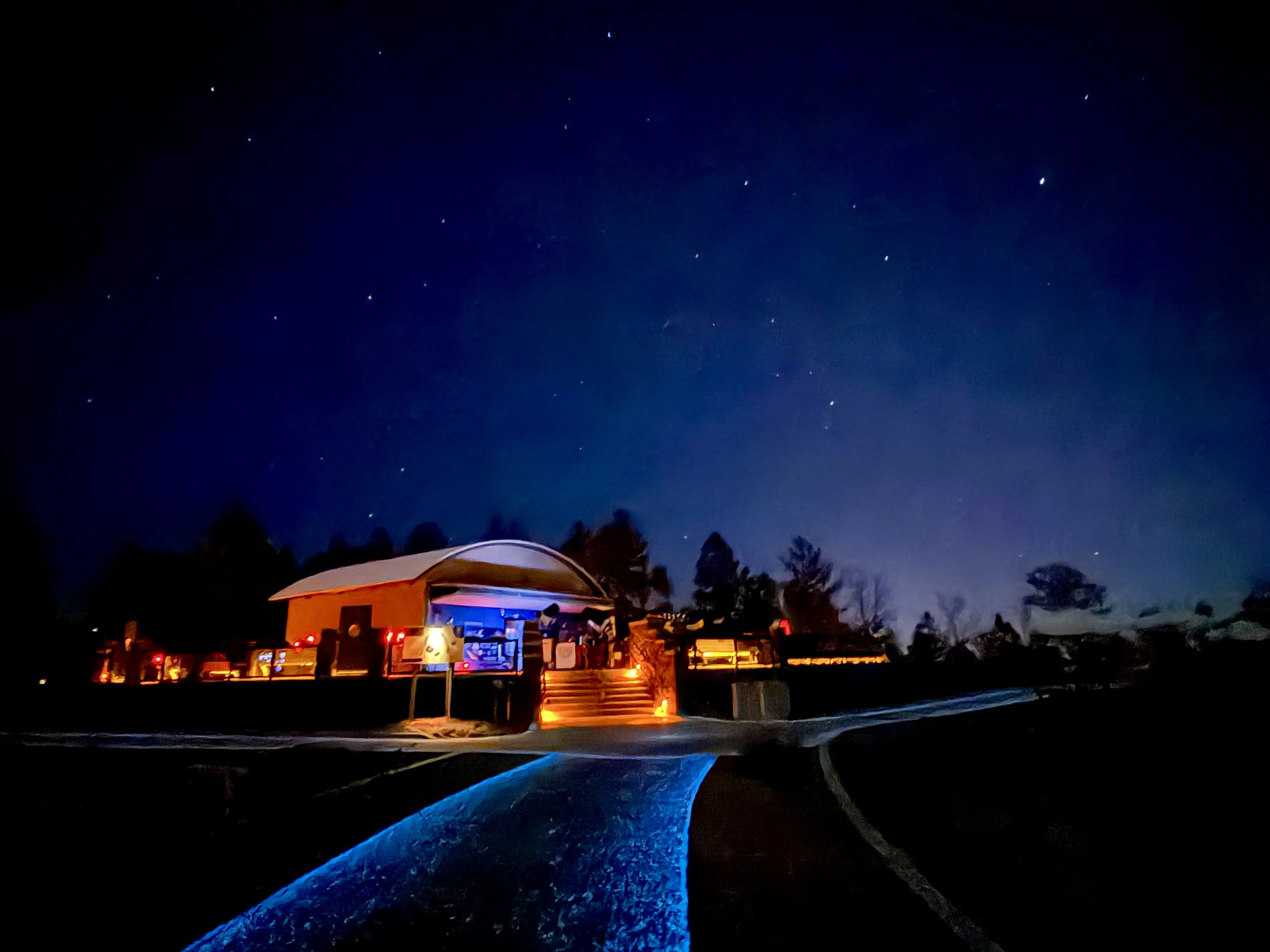 A walking path illuminated in blue leads to an oberservation area lit with red lights and set up with telescopes under the starry night sky