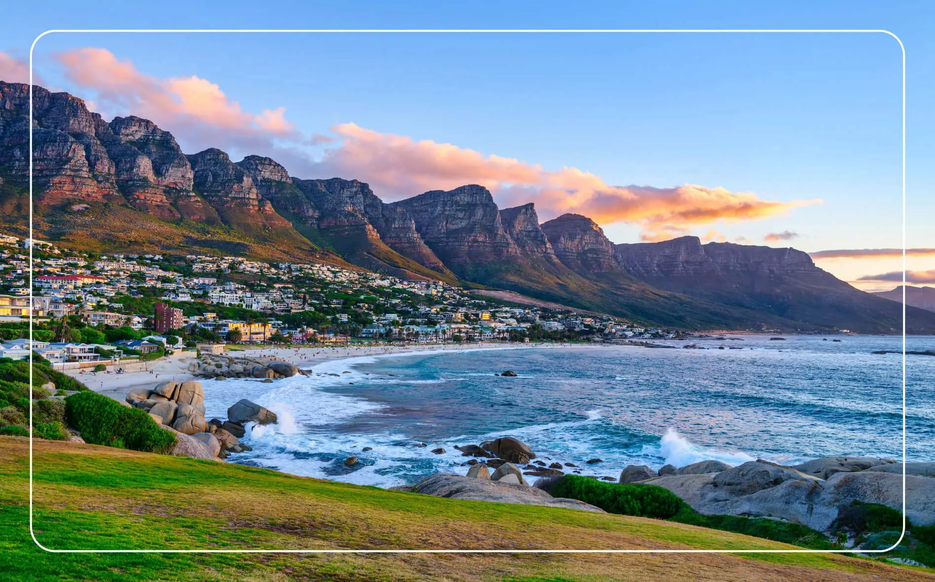 View of Cape Town at golden hour, with the coastline in the foreground and dramatic mountains rising in the background under warm, glowing light.