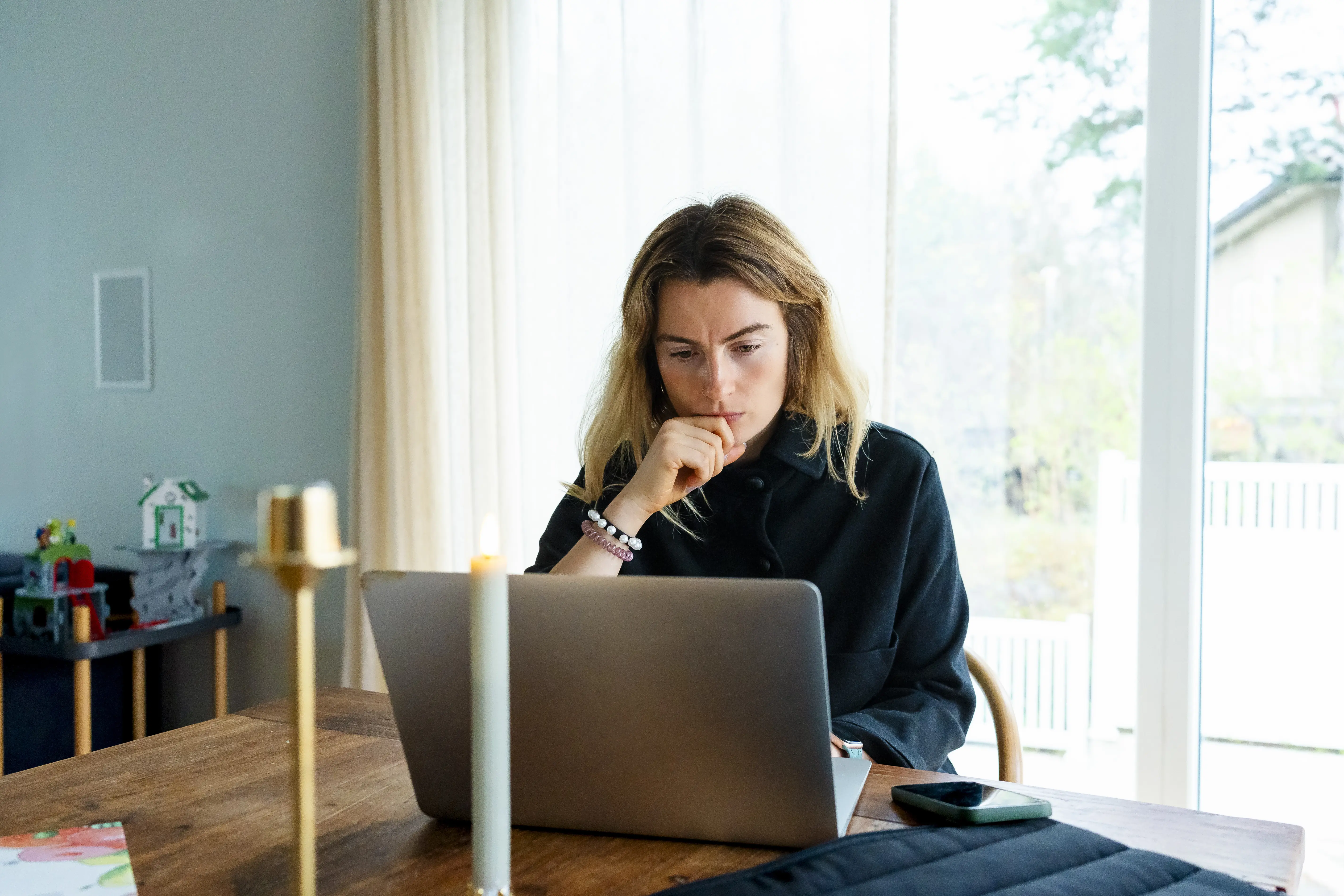Image of a woman sitting a counter using a laptop while thinking hard.