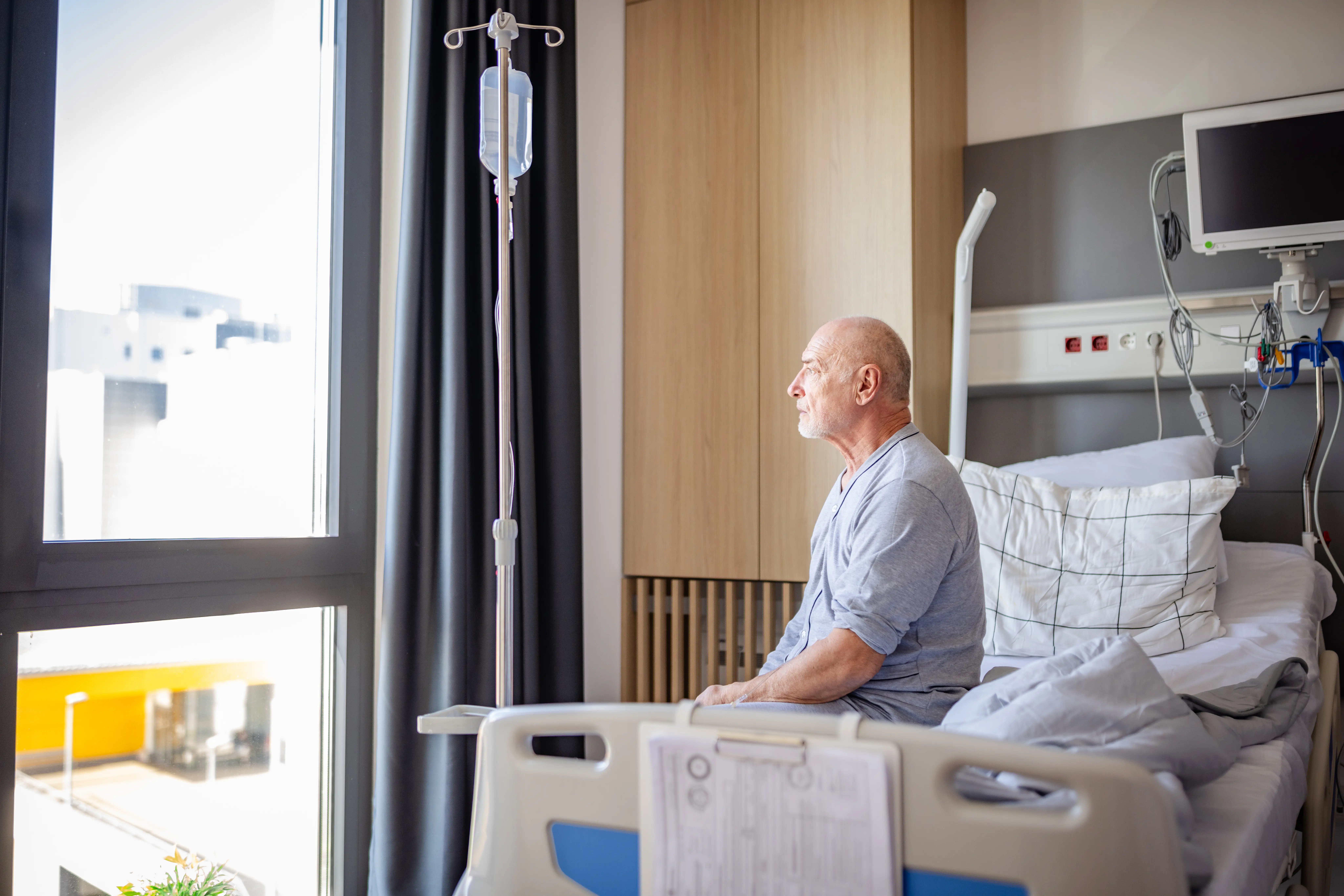 Image of a man looking reflective while sitting in a hospital bed.