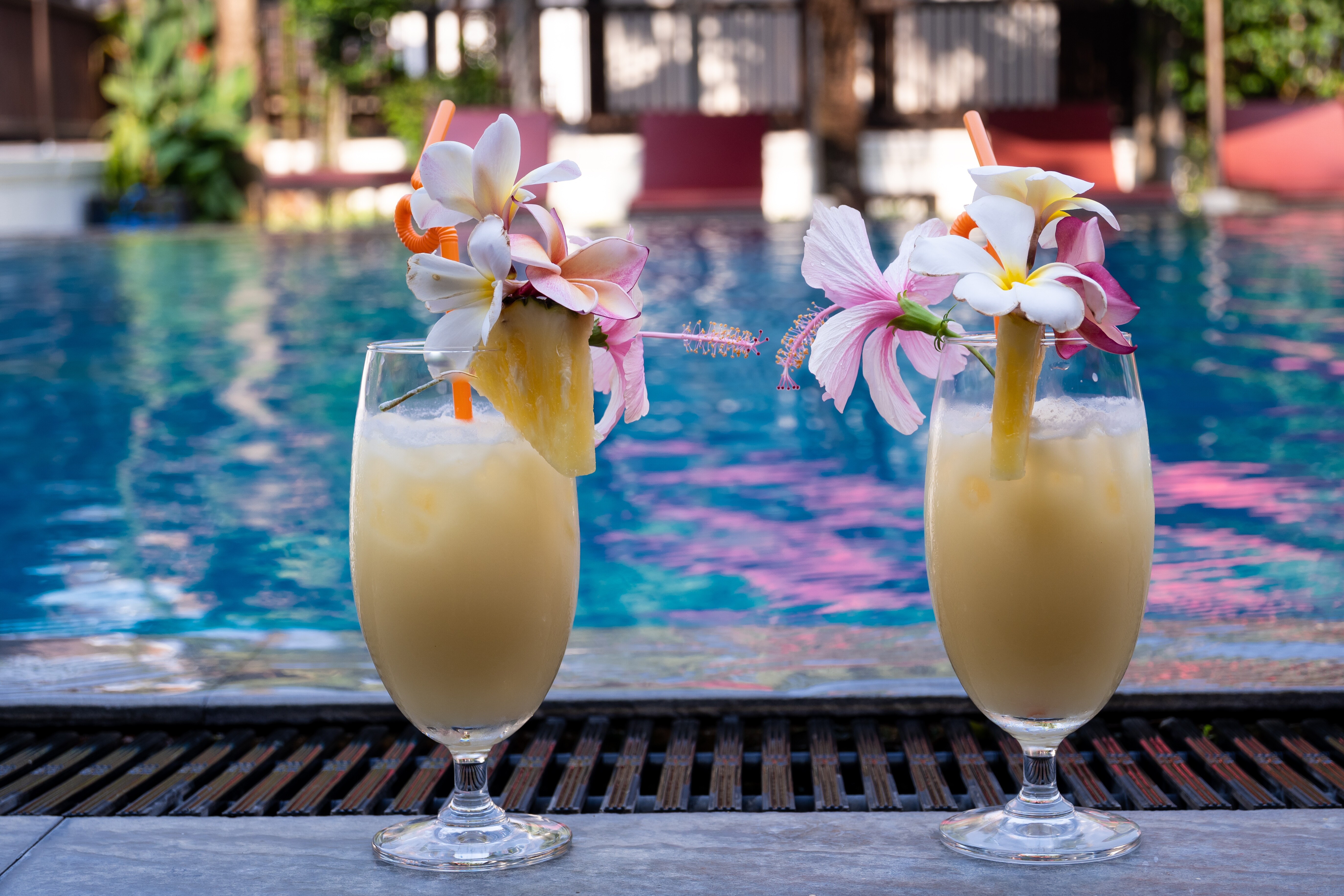 Image of two cocktail drinks sitting in front a swimming pool.
