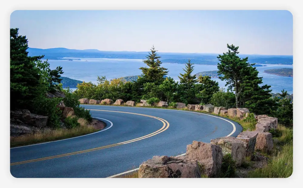 A curve on Park Loop Road with trees lining the road and views of the water in the background.