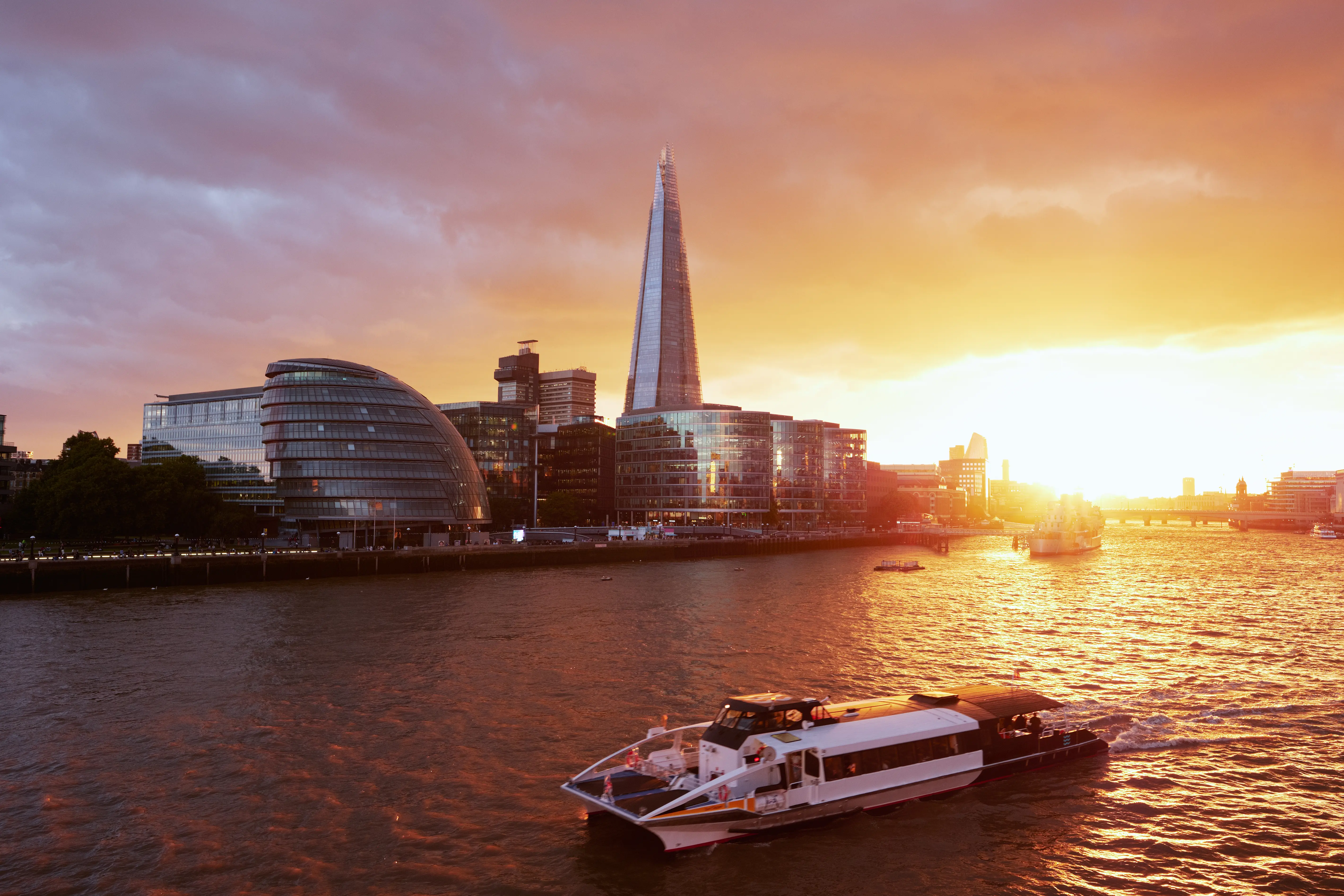 Image of the River Thames at sunset with a small cruise ship sailing in the foreground.
