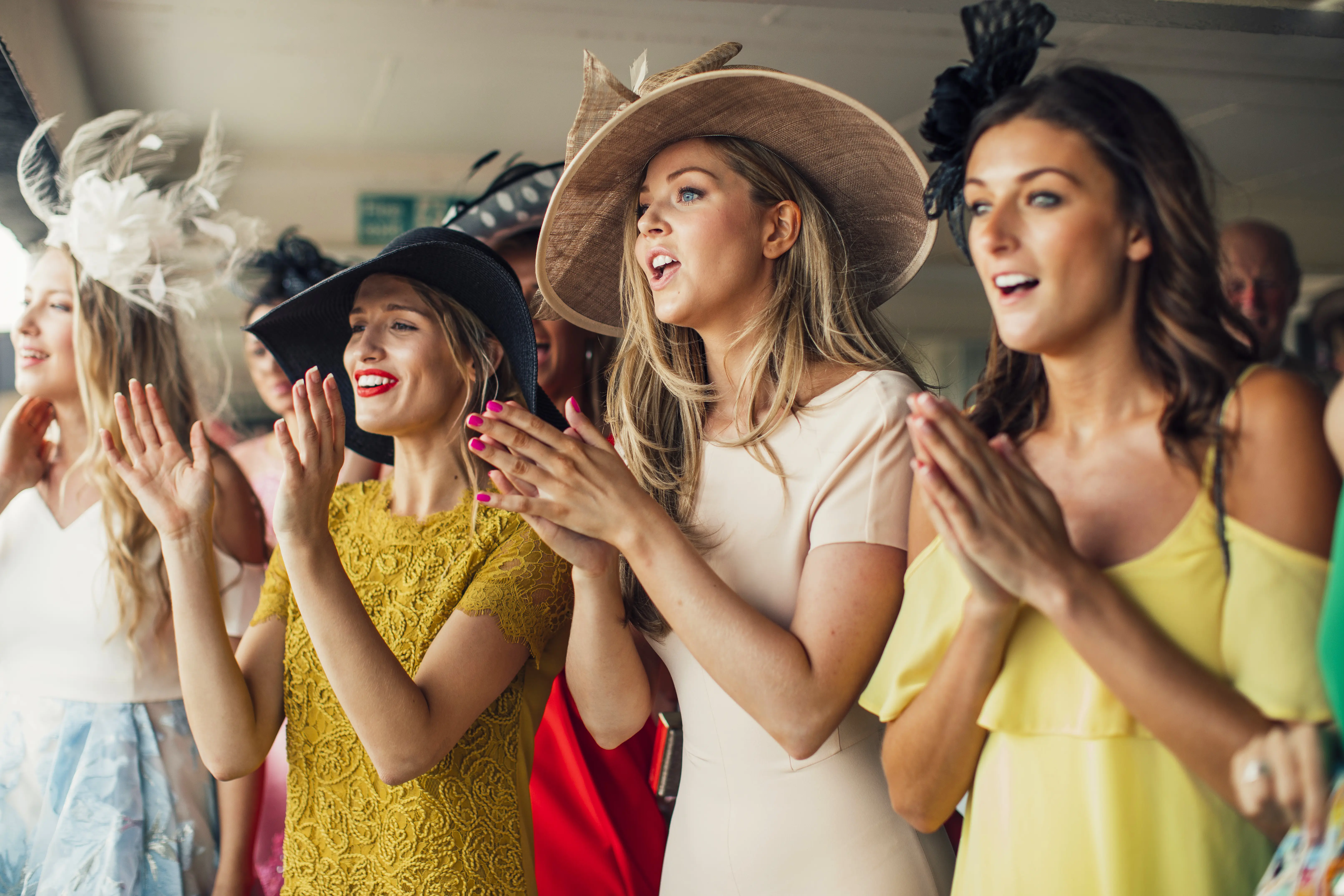 Group of well-dressed young ladies with fancy headwear and fascinators cheering at a horse race