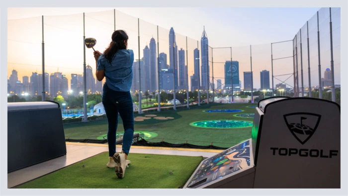 A woman swings a golf club while playing at TopGolf. 