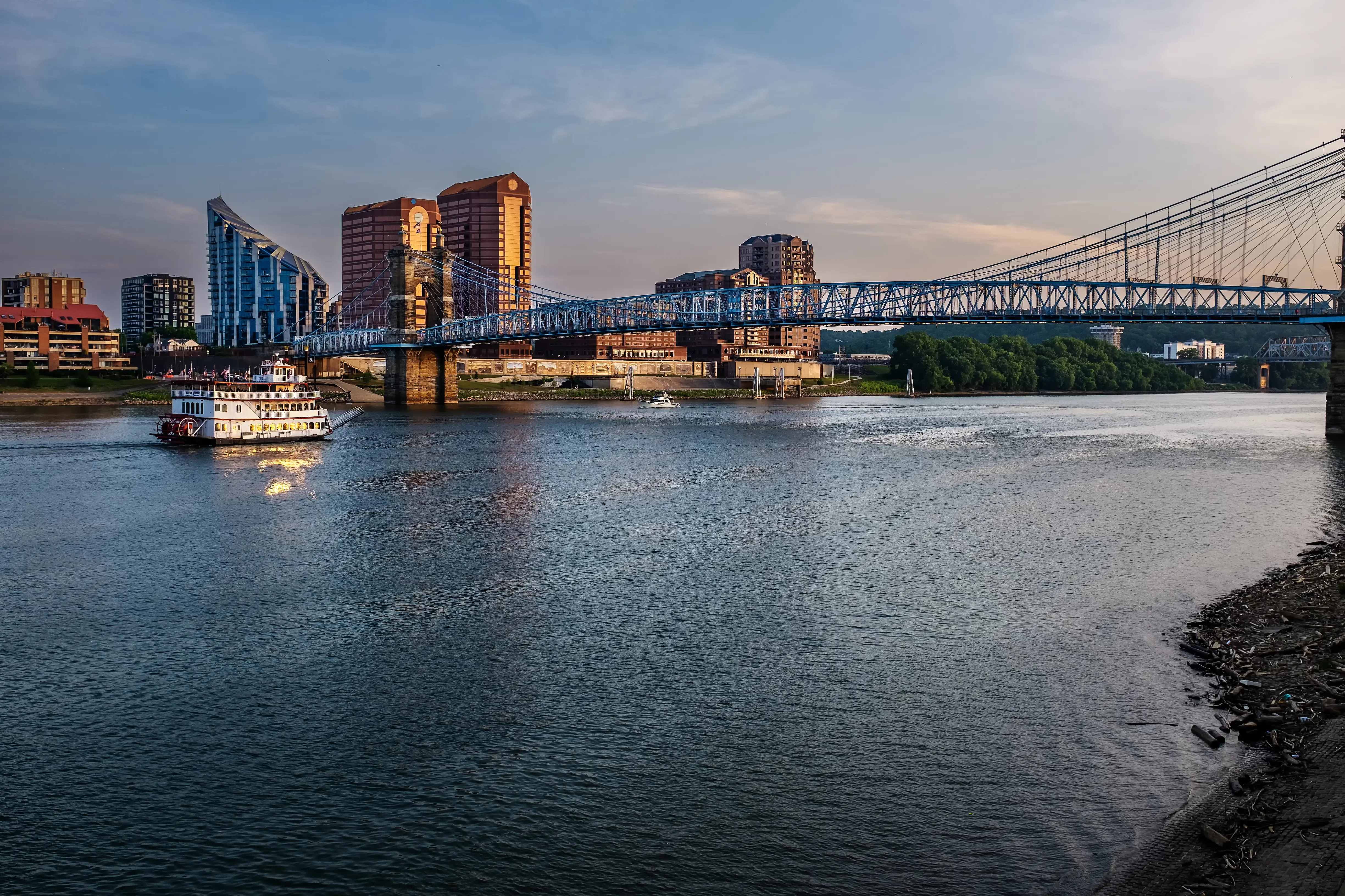 Image of a paddle boat river cruise sailing the Ohio River as it passes under old suspension bridge between Cincinnati, Ohio and Covington, Kentucky.