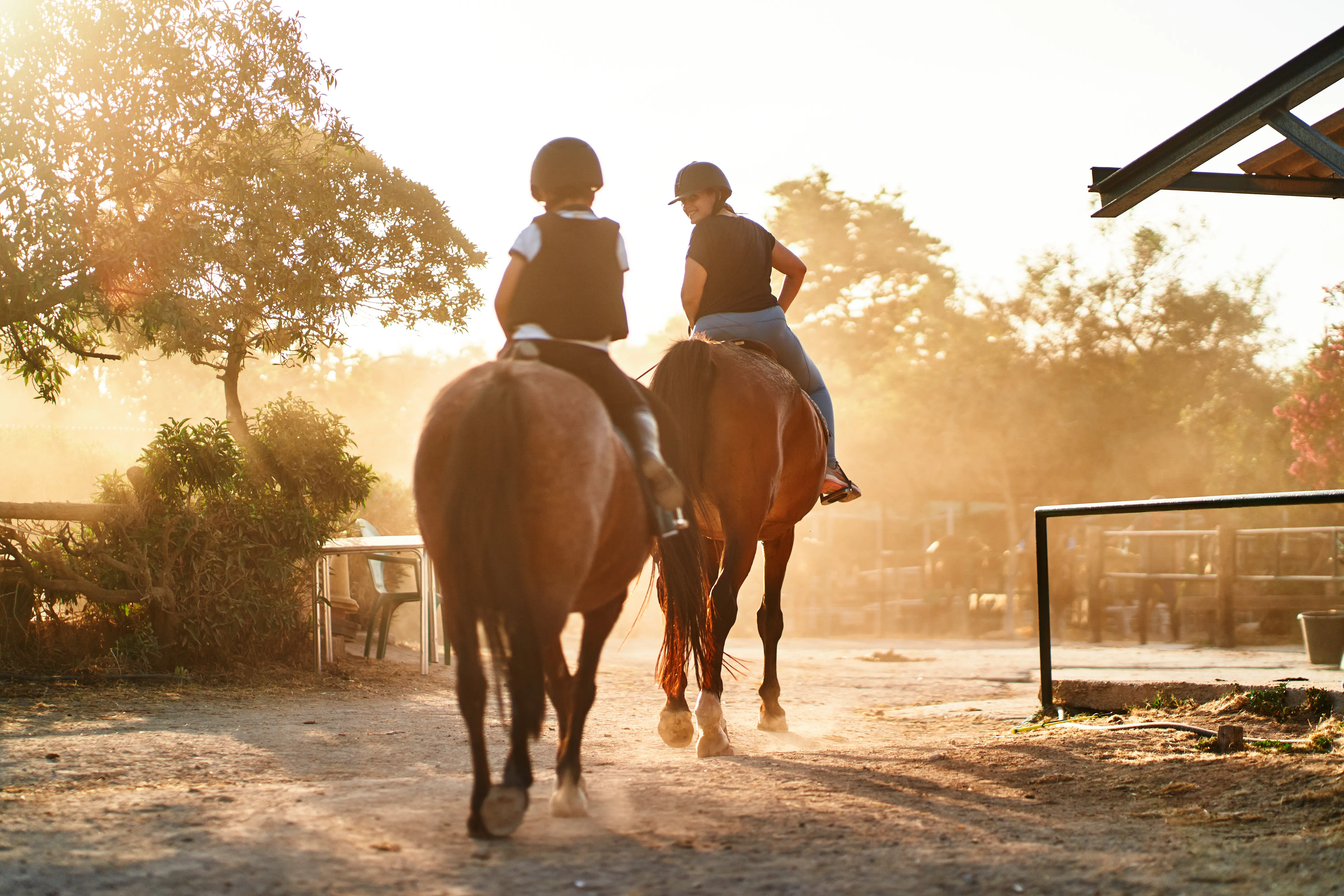 Image of two people going on a horseback ride on a dusty trail as the sun sets.