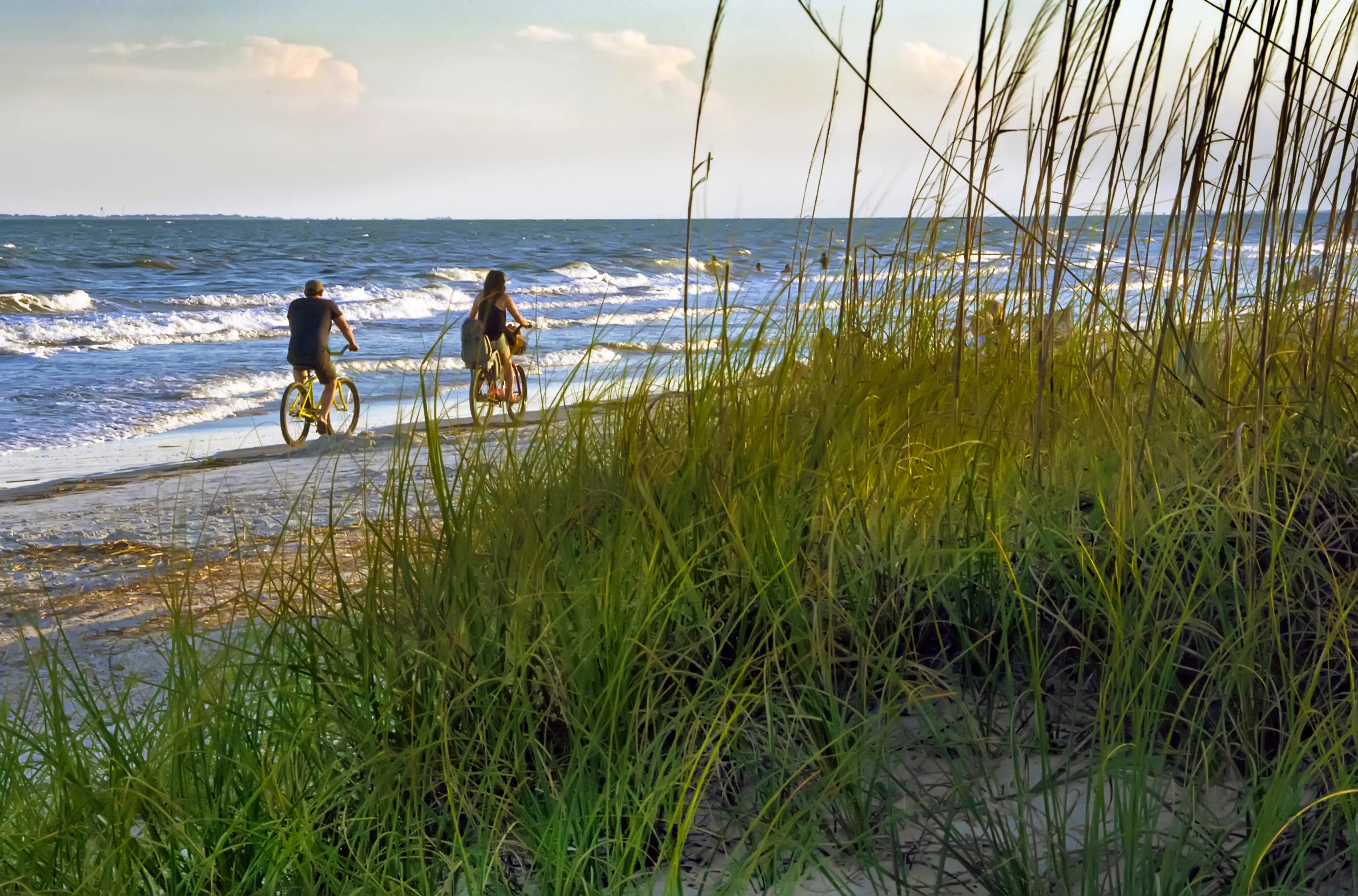 Couple riding their bikes along the beach between the dunes and surf on Hilton Head Island