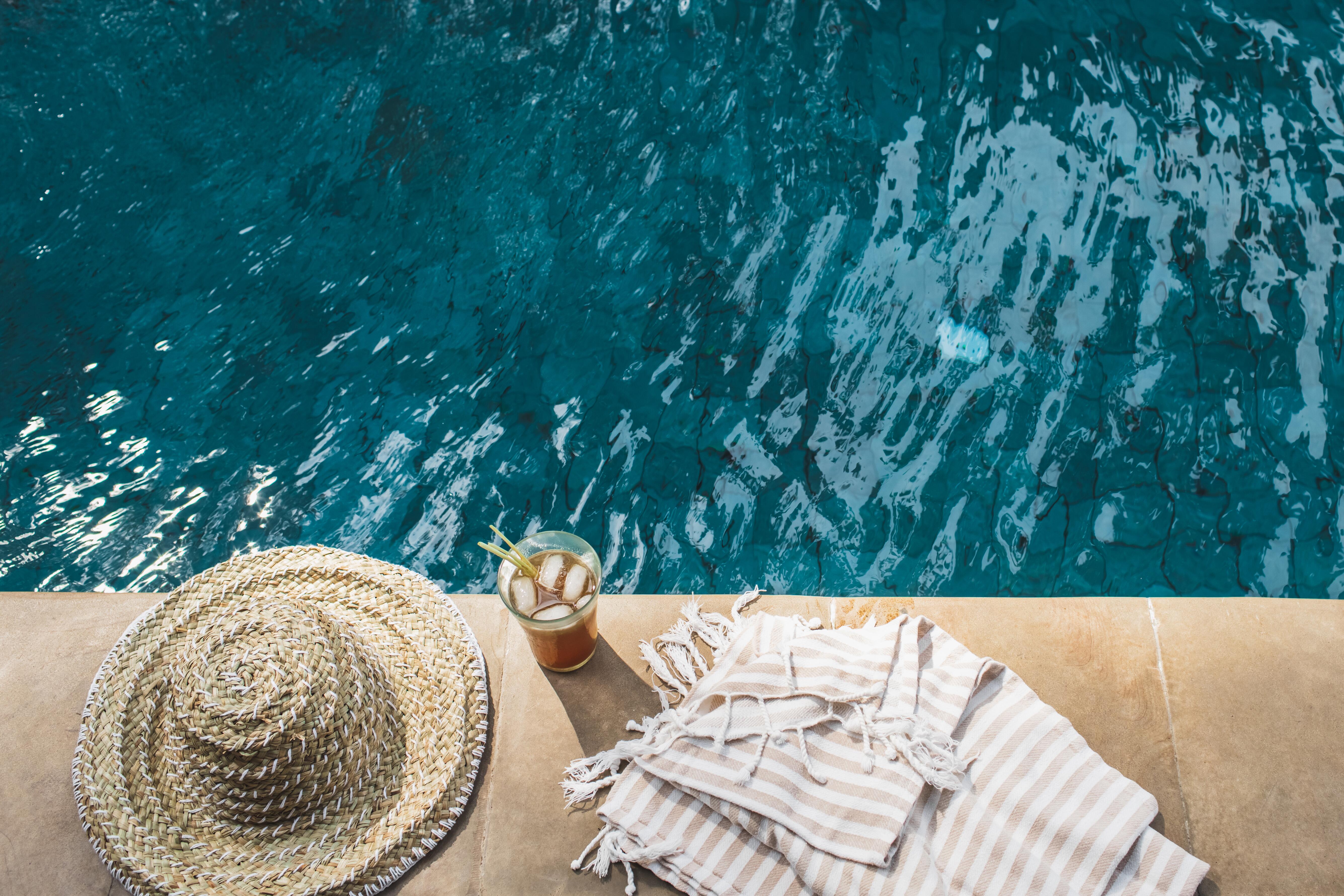 Image of beach/lounge items sitting as the side of a swimming pool.