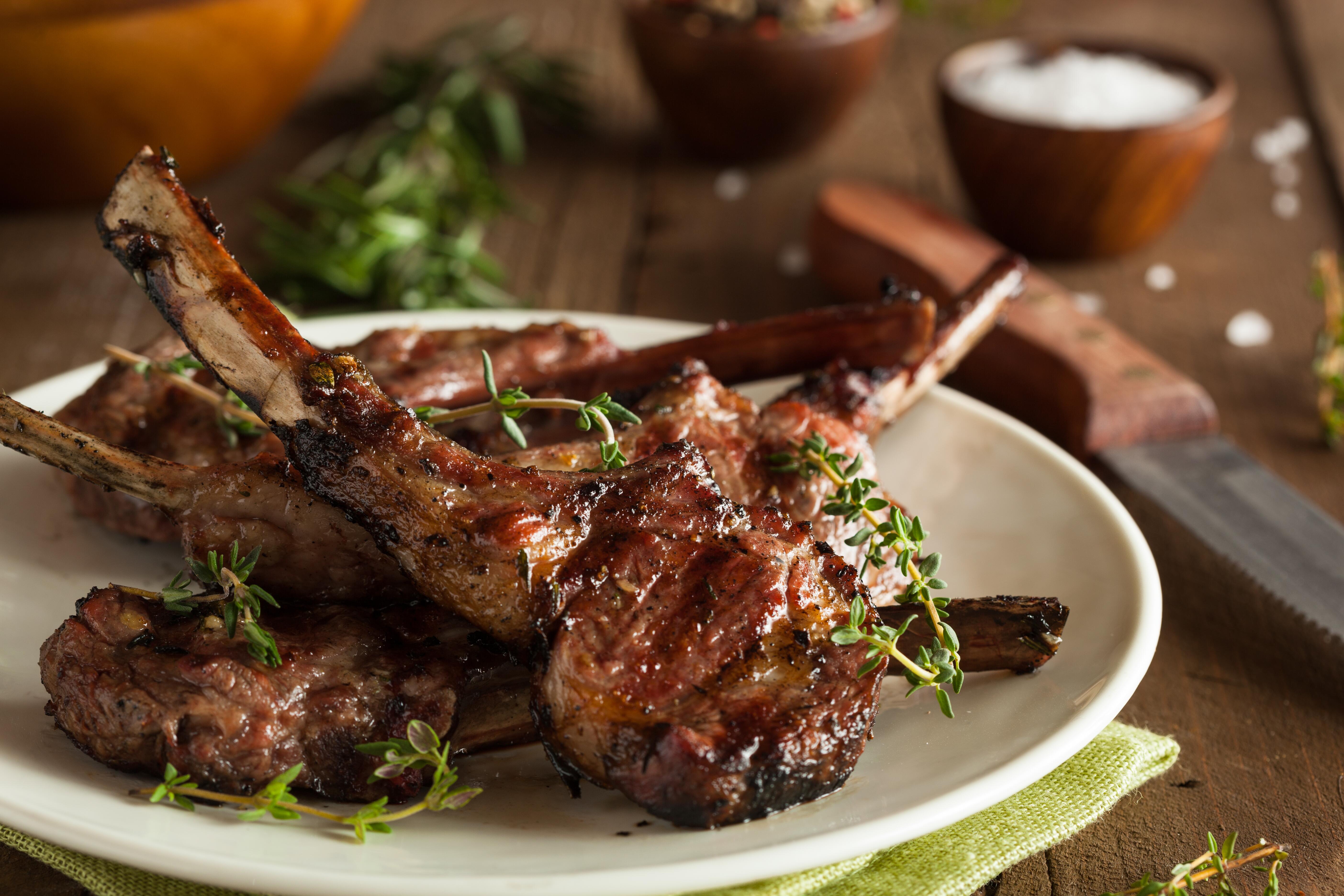 Grilled lamb chops organized on a white plate on wood table