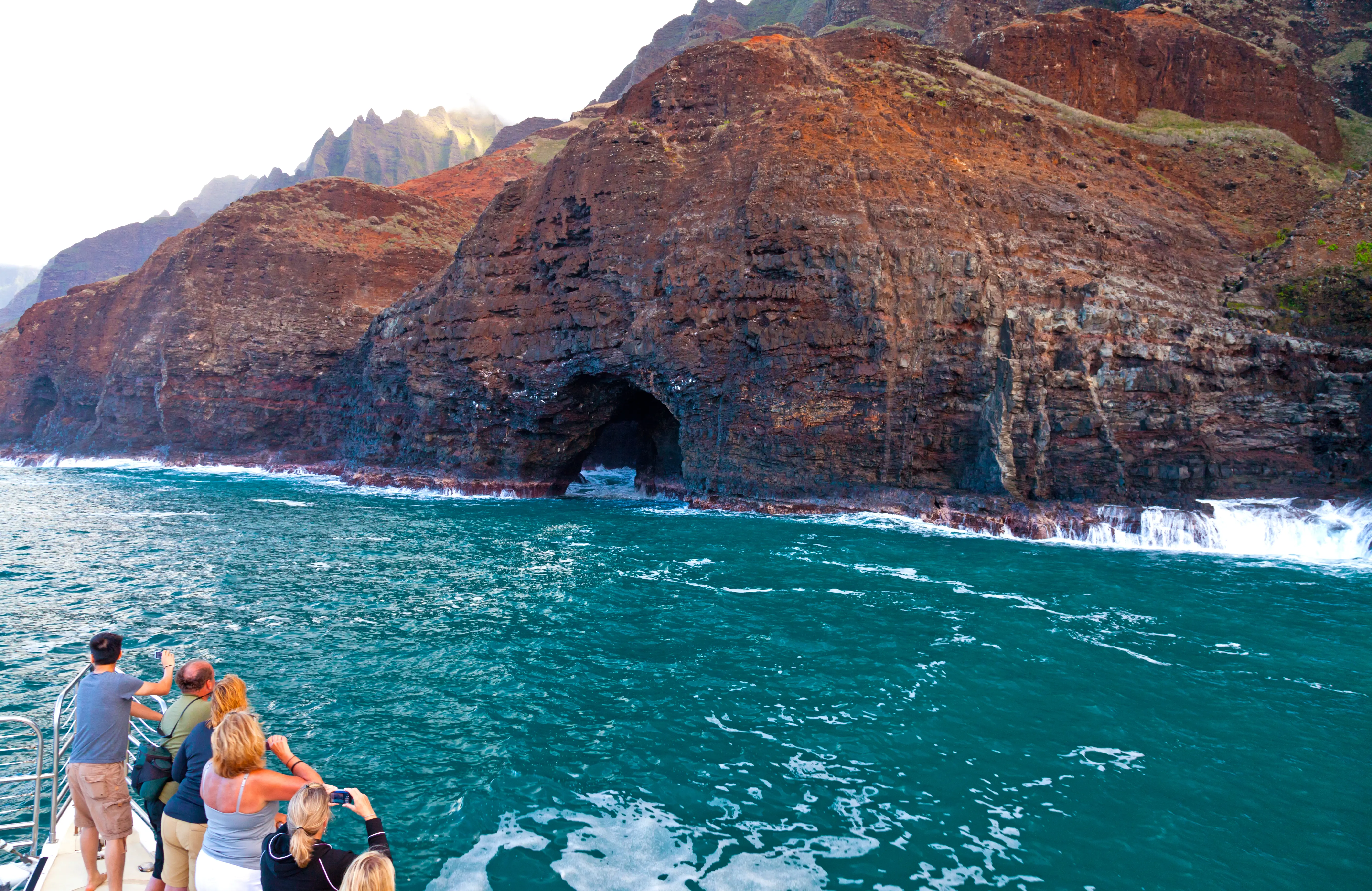 Tourists taking pictures of the cliffs and caves of Napali Coast