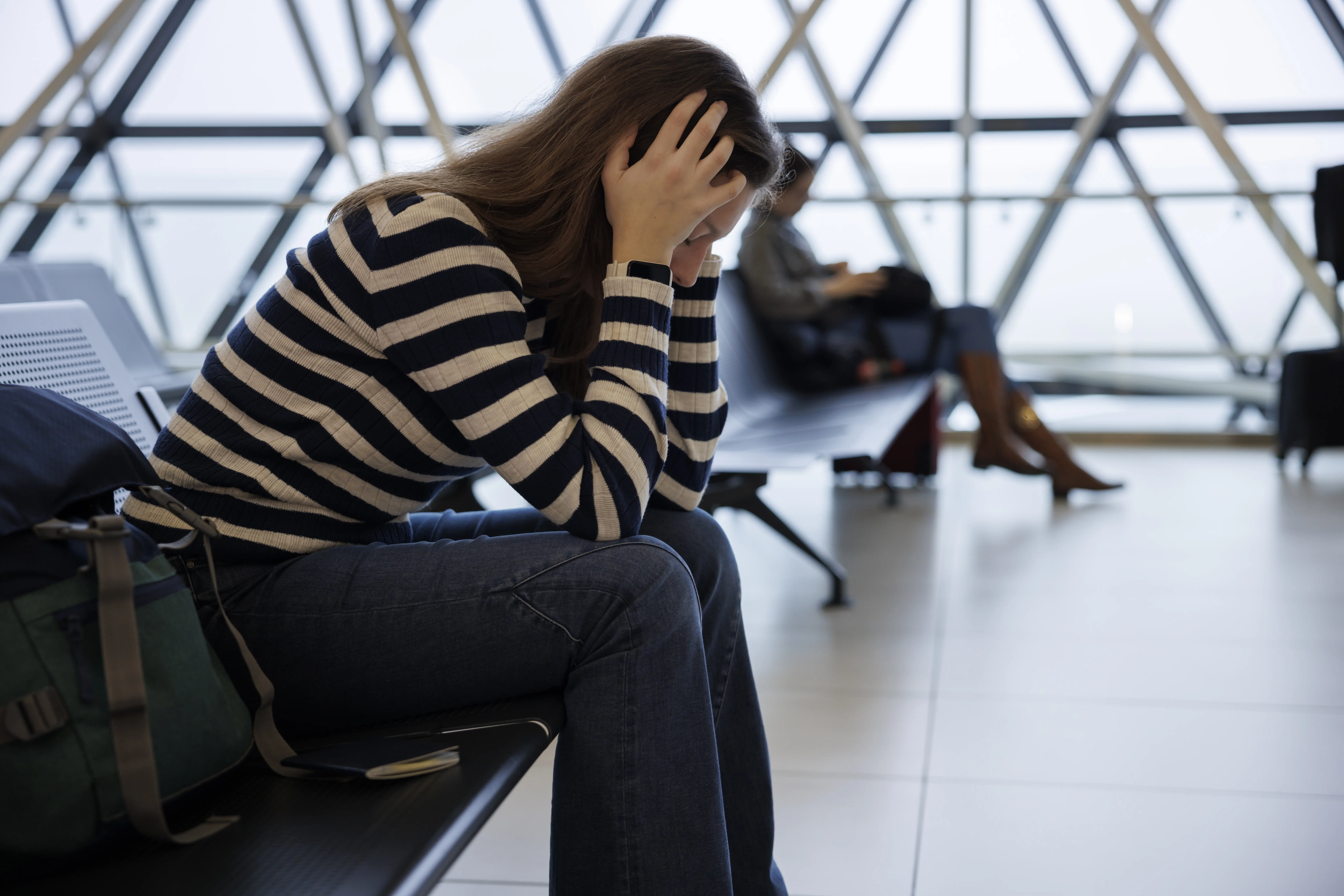 Image of woman sitting at an airport terminal looking frustrated.