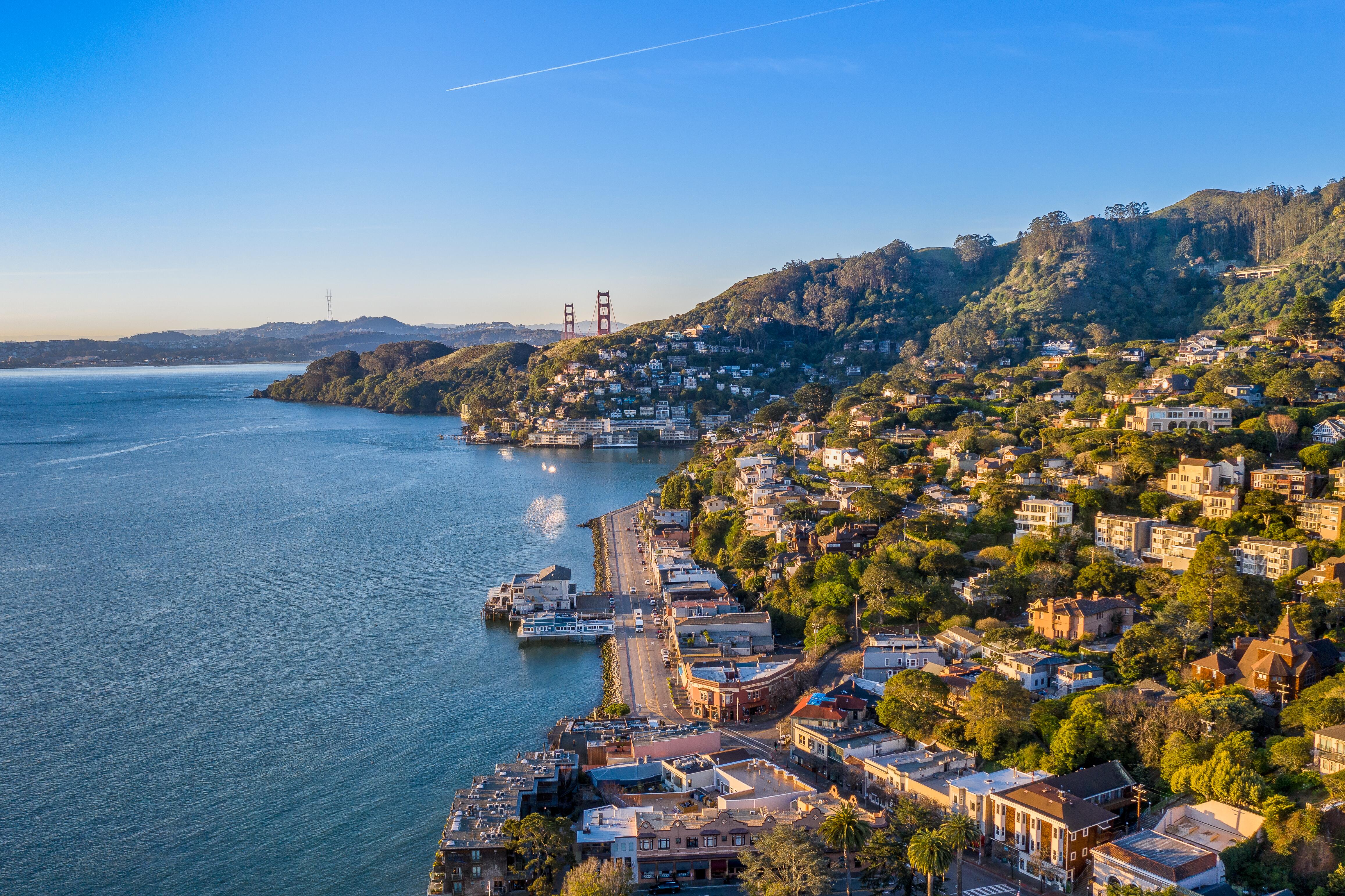 Image of the city of Sausalito from above, with the Golden Gate Bridge visible in the distance.