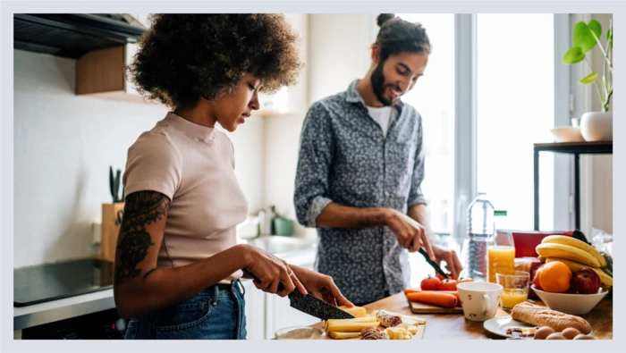 A couple stands in their kitchen chopping food for dinner.