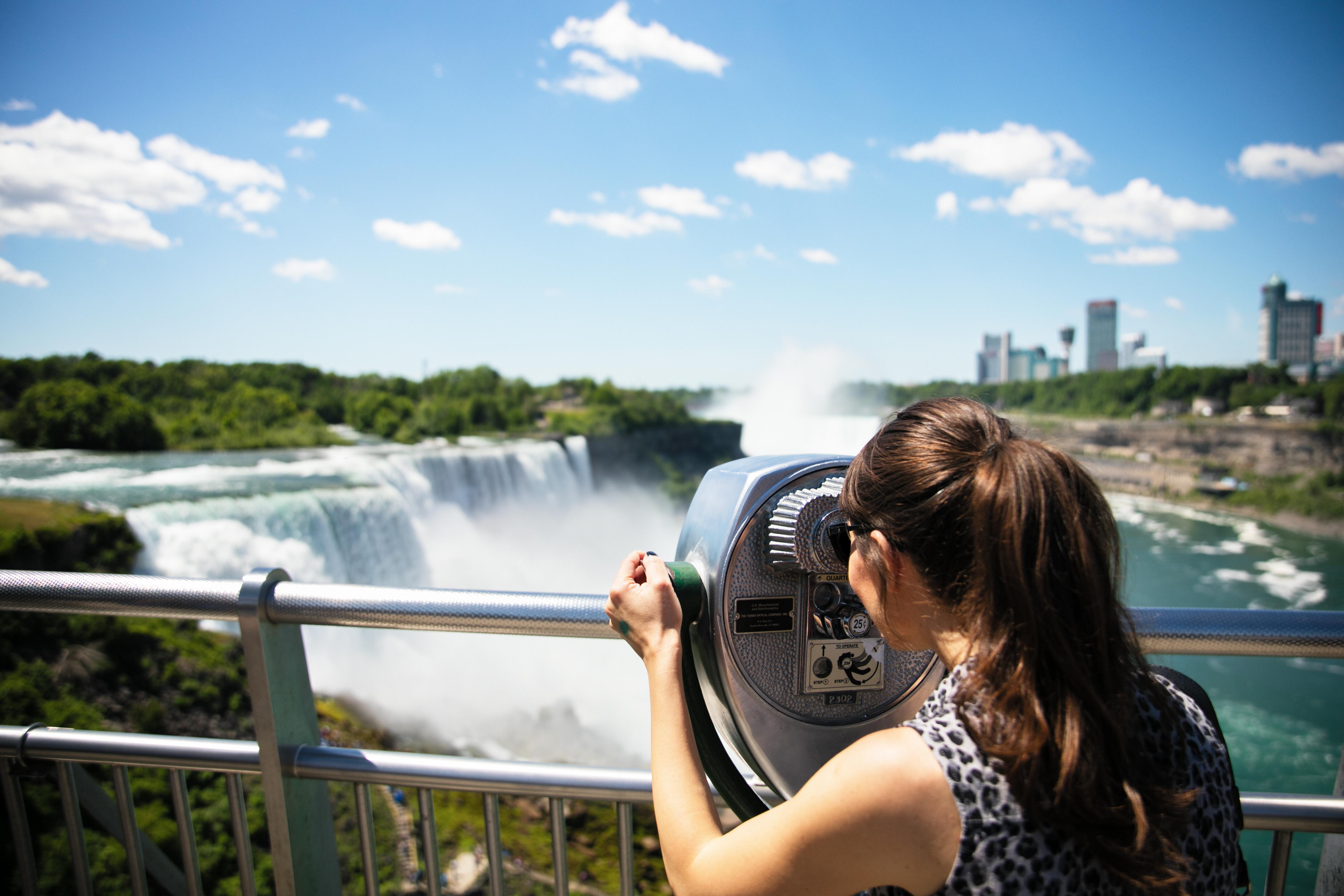 Woman tourist enjoying beautiful view of Niagara Fall through coin operated binoculars from USA side