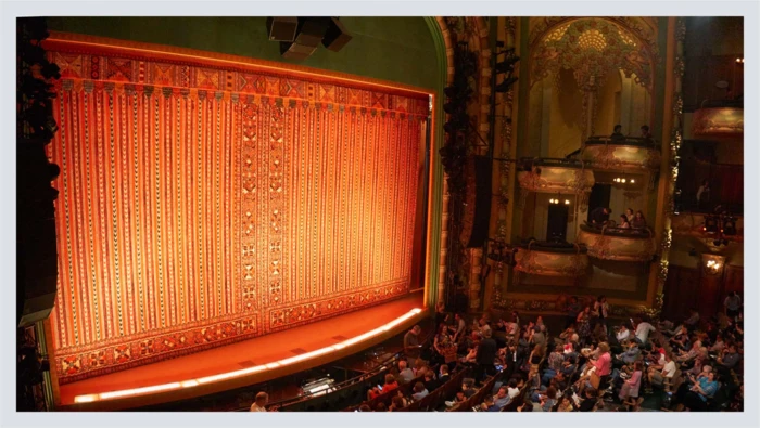 A crowd sits in an ornate theater facing the stage before the show begins.