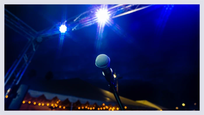 A closeup shot of a microphone on a lit stage is shown, alluding to the experience gift of comedy club tickets. 