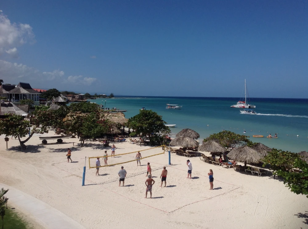 People playing beach volleyball by the ocean at Sandals Montego Bay.
