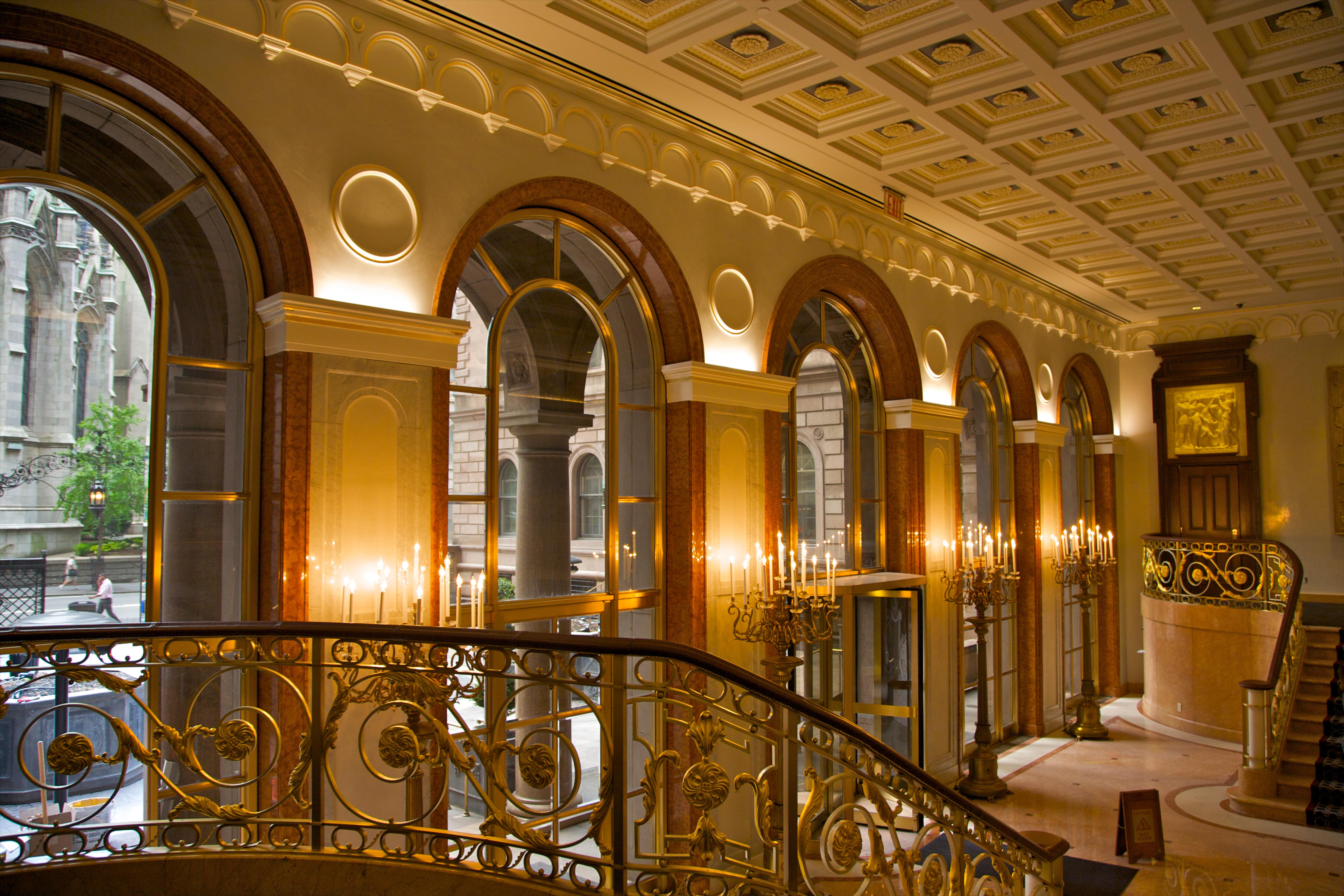 Warm light view of grillwork and chandeliers with large curved top windows and ornate staircase in the hotel lobby of the New York Palace Hotel, originally Villard Mansion, built 1883