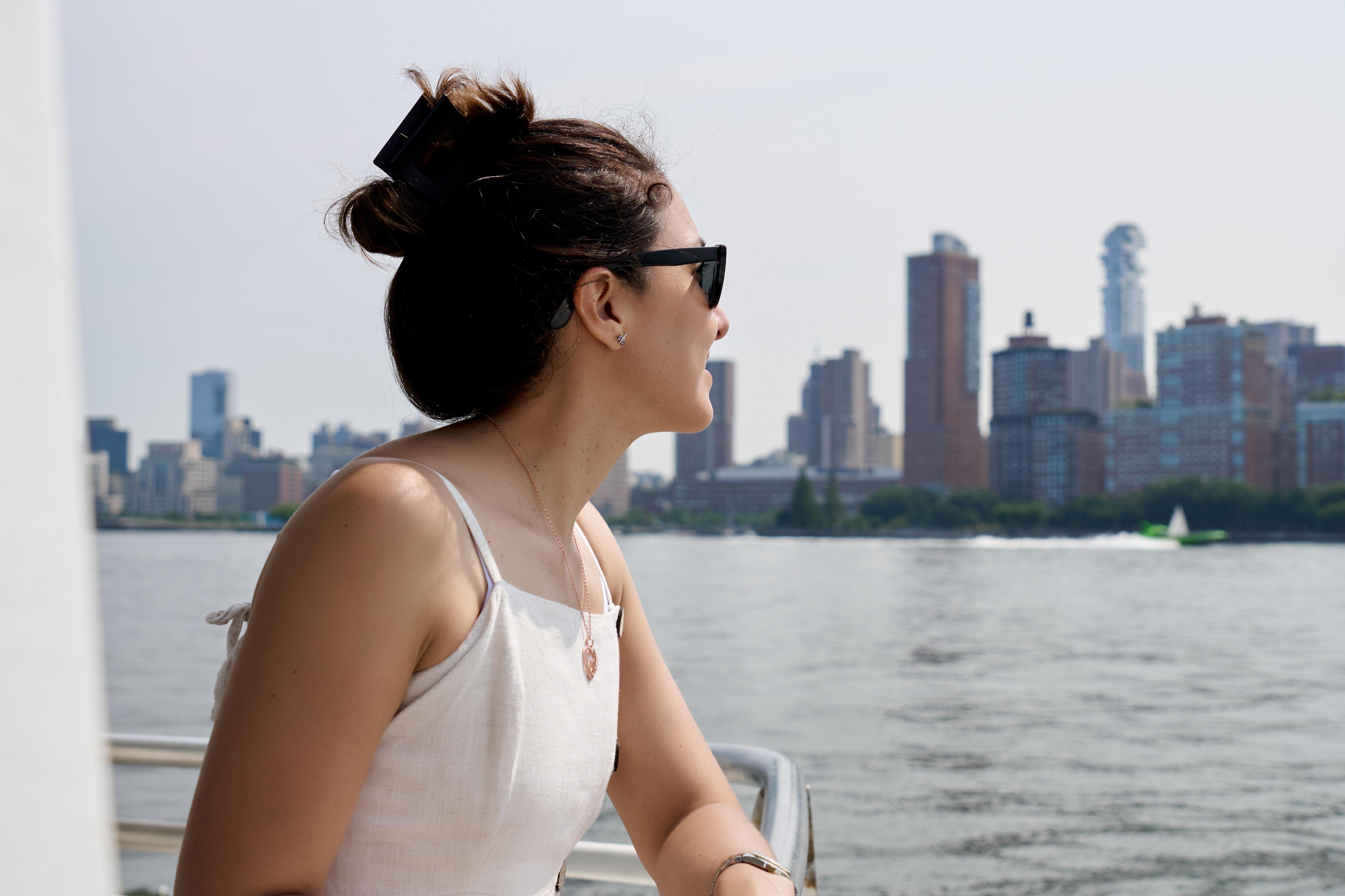 Image of a woman looking over the deck of a boat at a view of the New York City skyline.