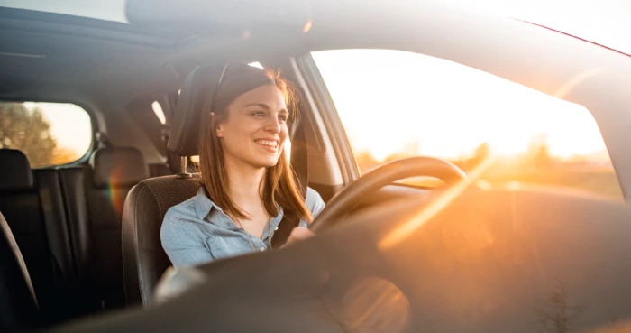 Smiling young woman driving on a country road during a sunset.