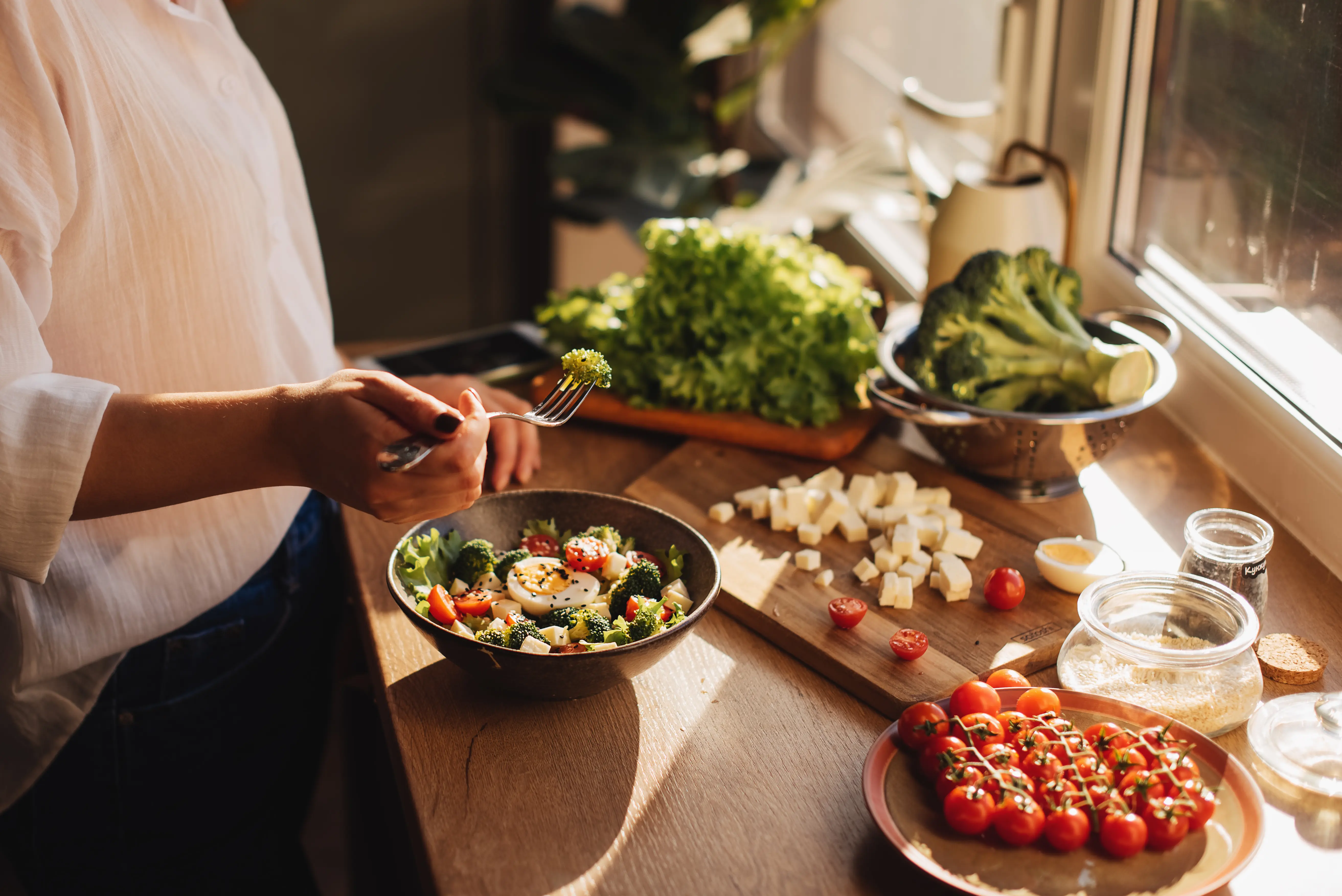 Image of a woman making a bowl dish with hummus, vegetable, salad, beans, couscous and avocado.