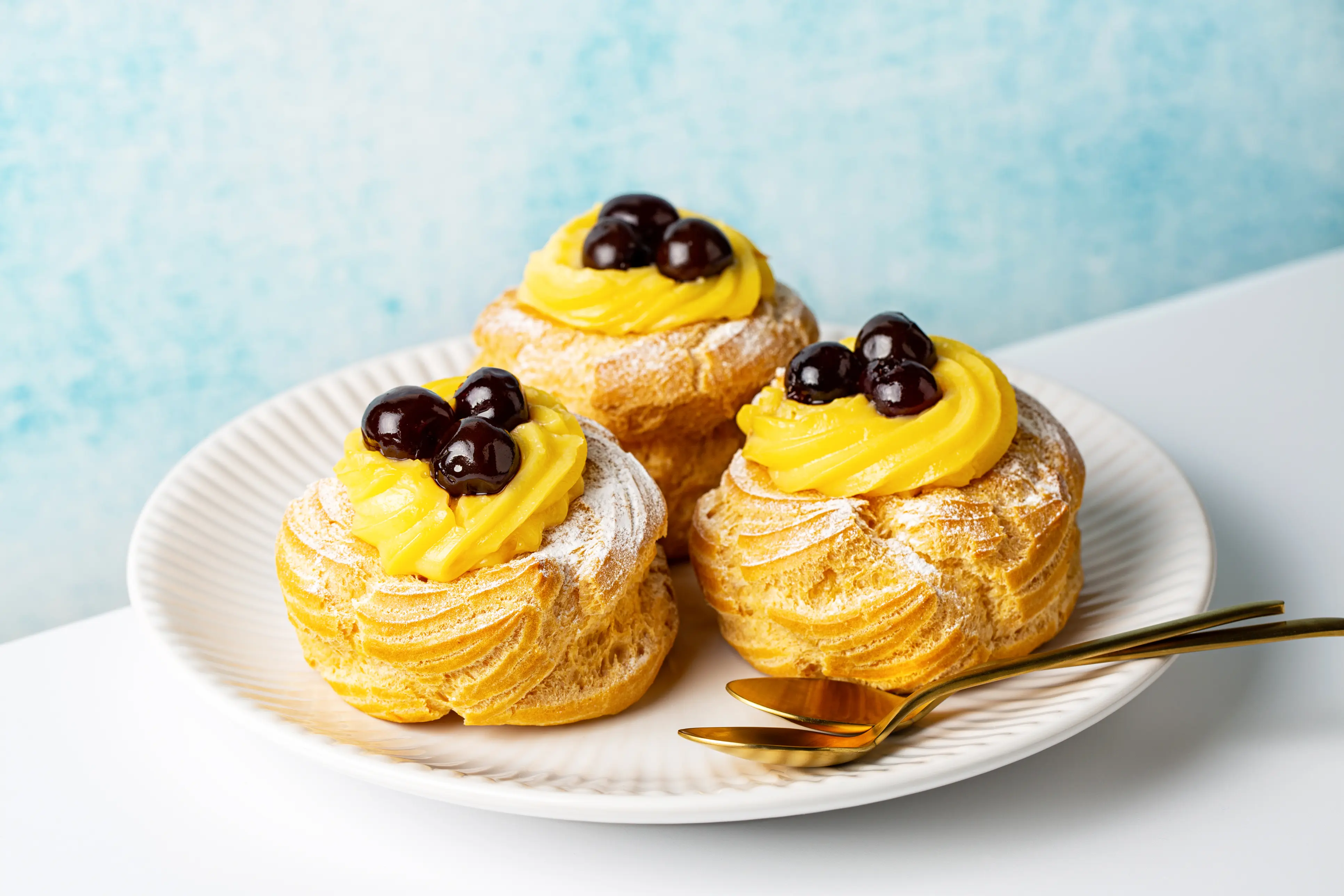 Zeppoles dusted with powdered sugar, decorated and filled with custard cream, and topped with Amarena cherries