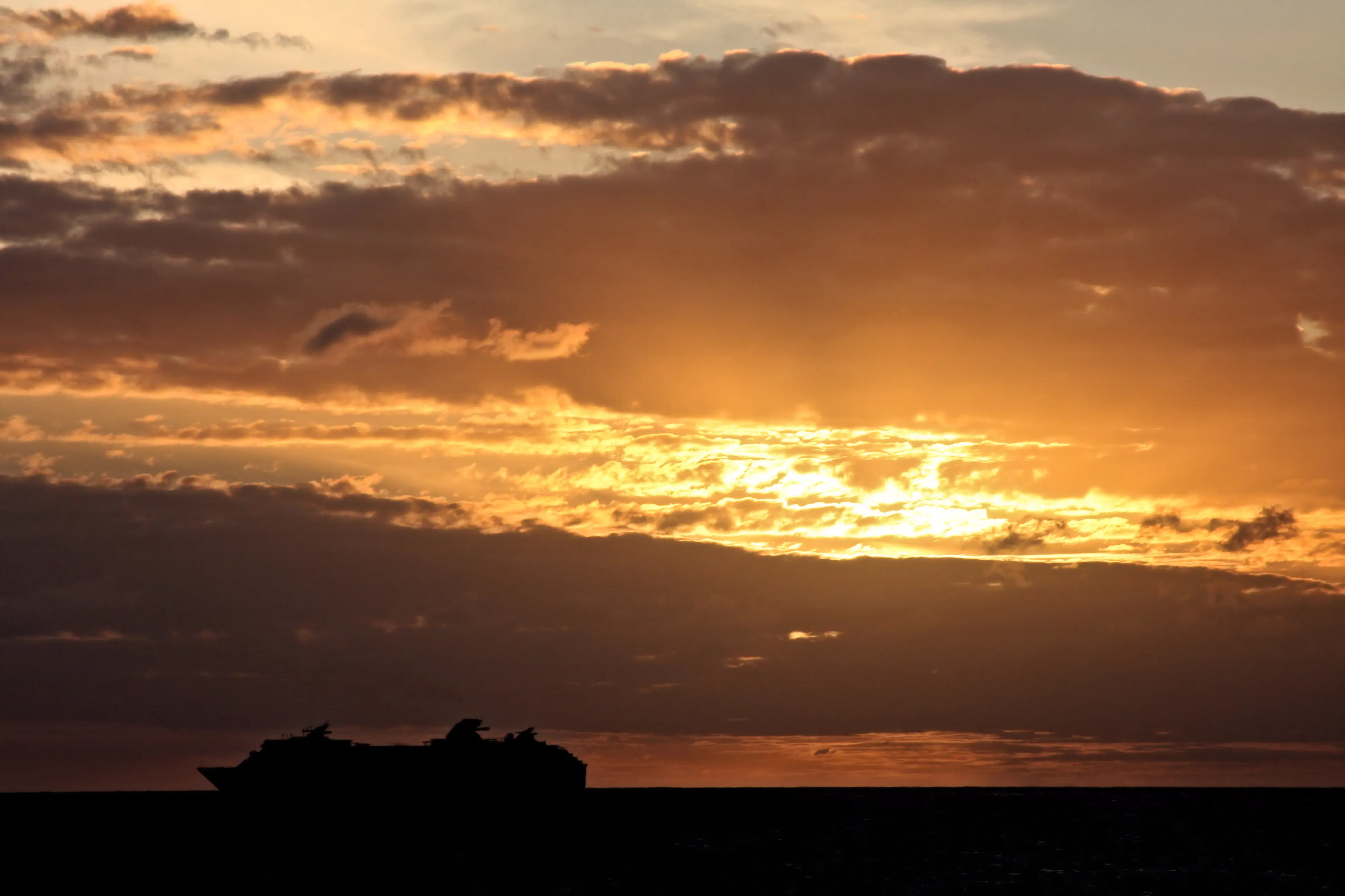 Image of the Celebrity Summit cruise ship silhouetted by the sunset behind it as it sails.