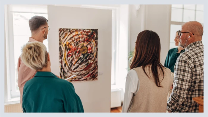 A group of people take part in an art gallery tour inside of an art museum as they gaze at a painting. 