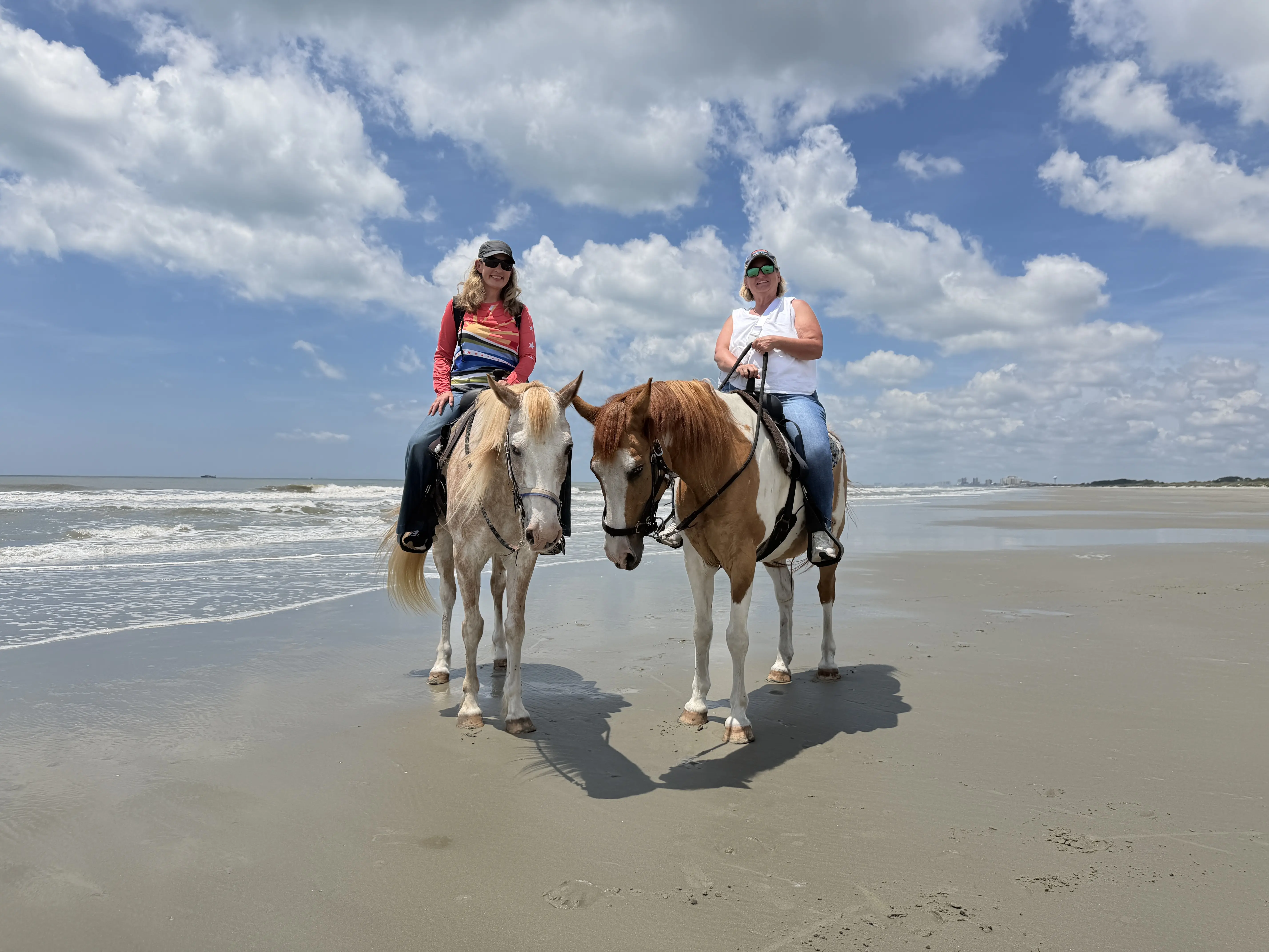 Two women sitting atop horsed standing on a beach on a sunny day