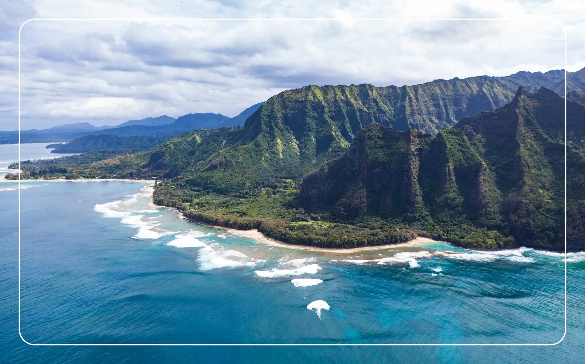 Waves crash along the shore of the green and mountainous Nā Pali Coastline.