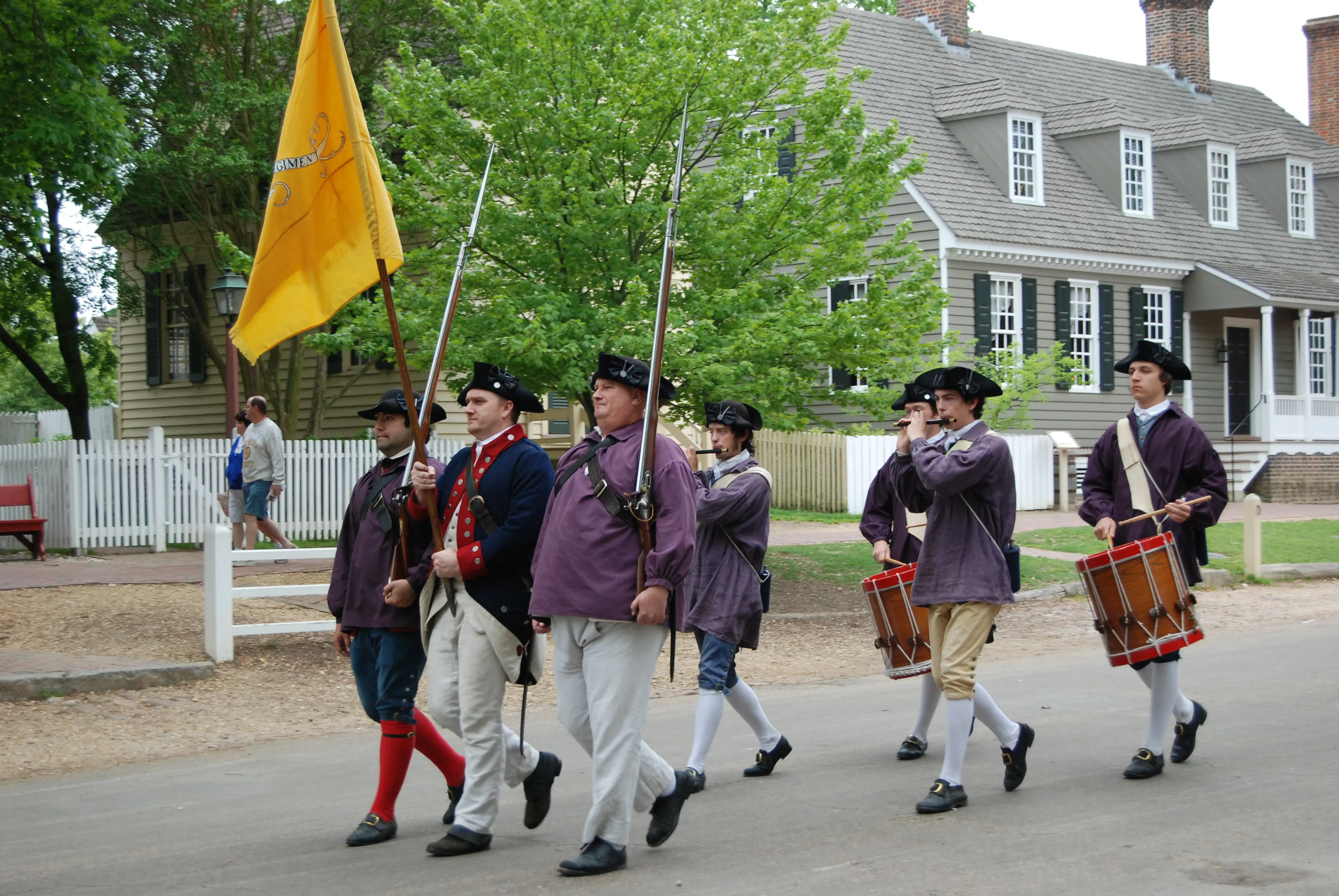 Image of people in Colonial Williamsburg reenacting troops and a band walking through the street.