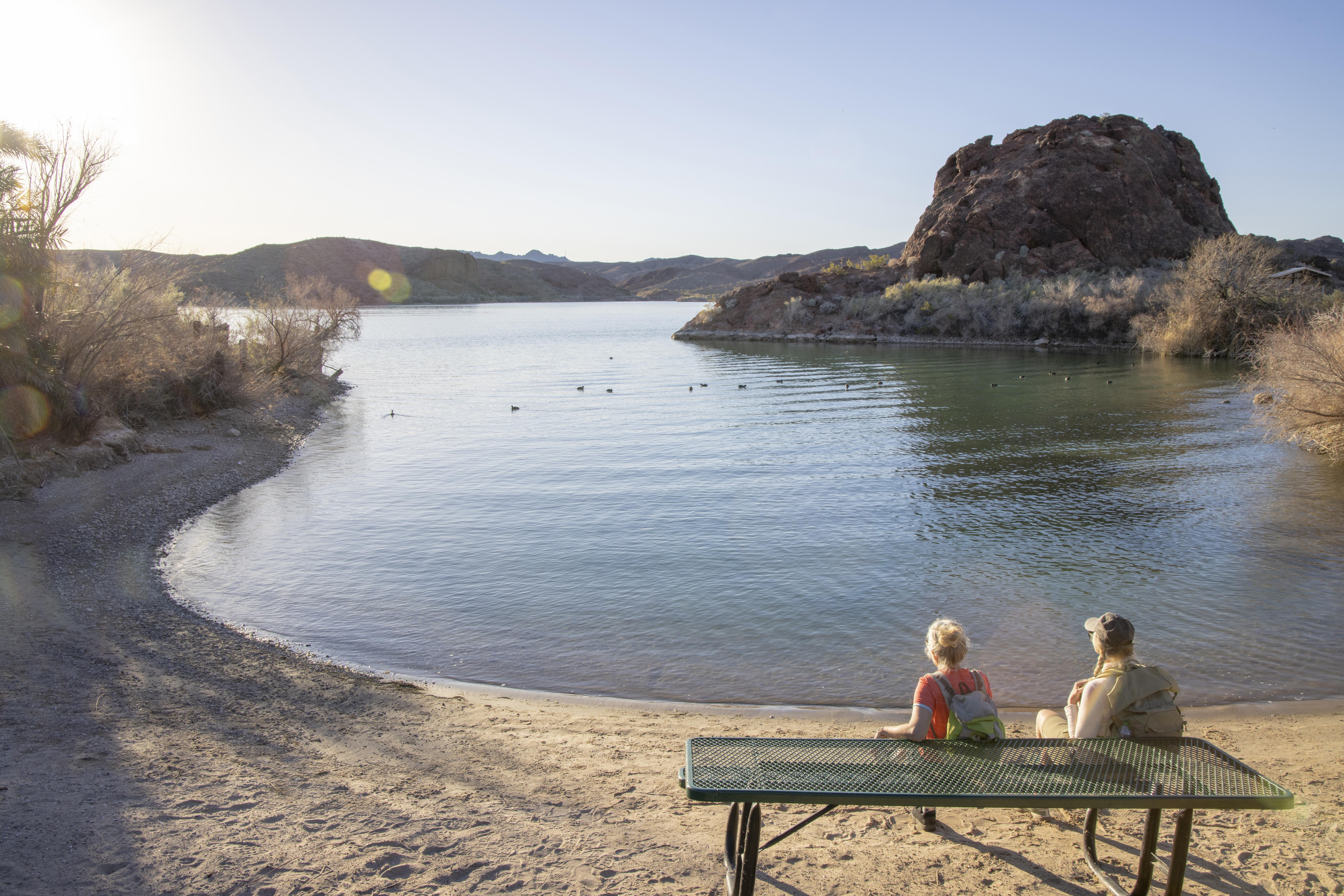 Image of hikers sitting on a bench by the shore of Lake Havasu, California.