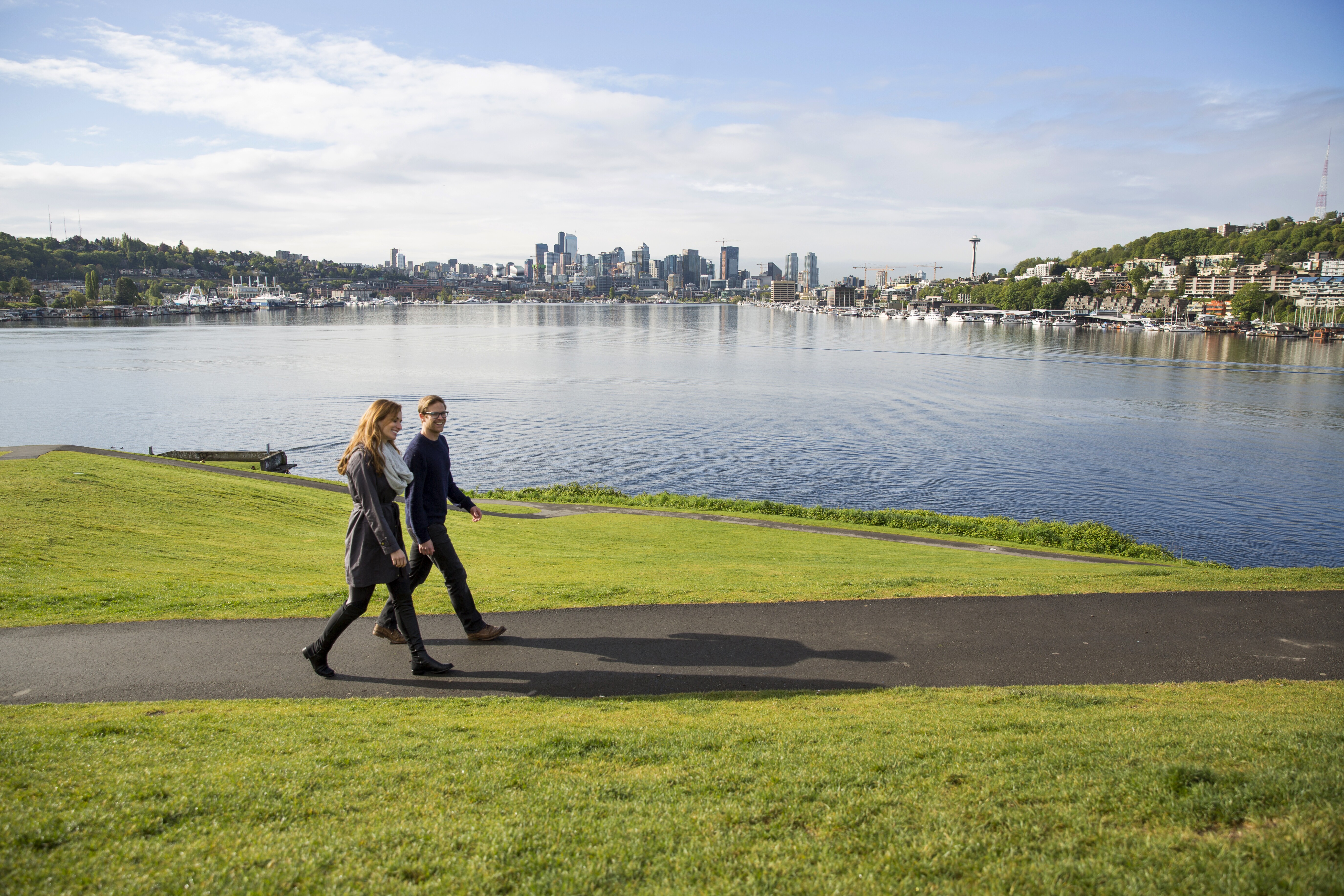 Image of two people walking in a park setting with the Seattle skyline in the distance.