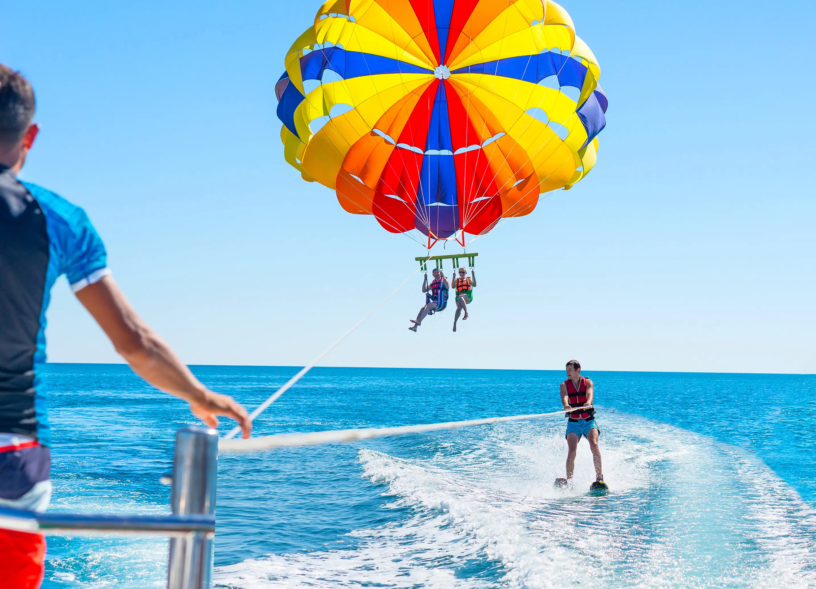 Boat pulling a couple parasailing in the air and a young man waterskiing on the waves