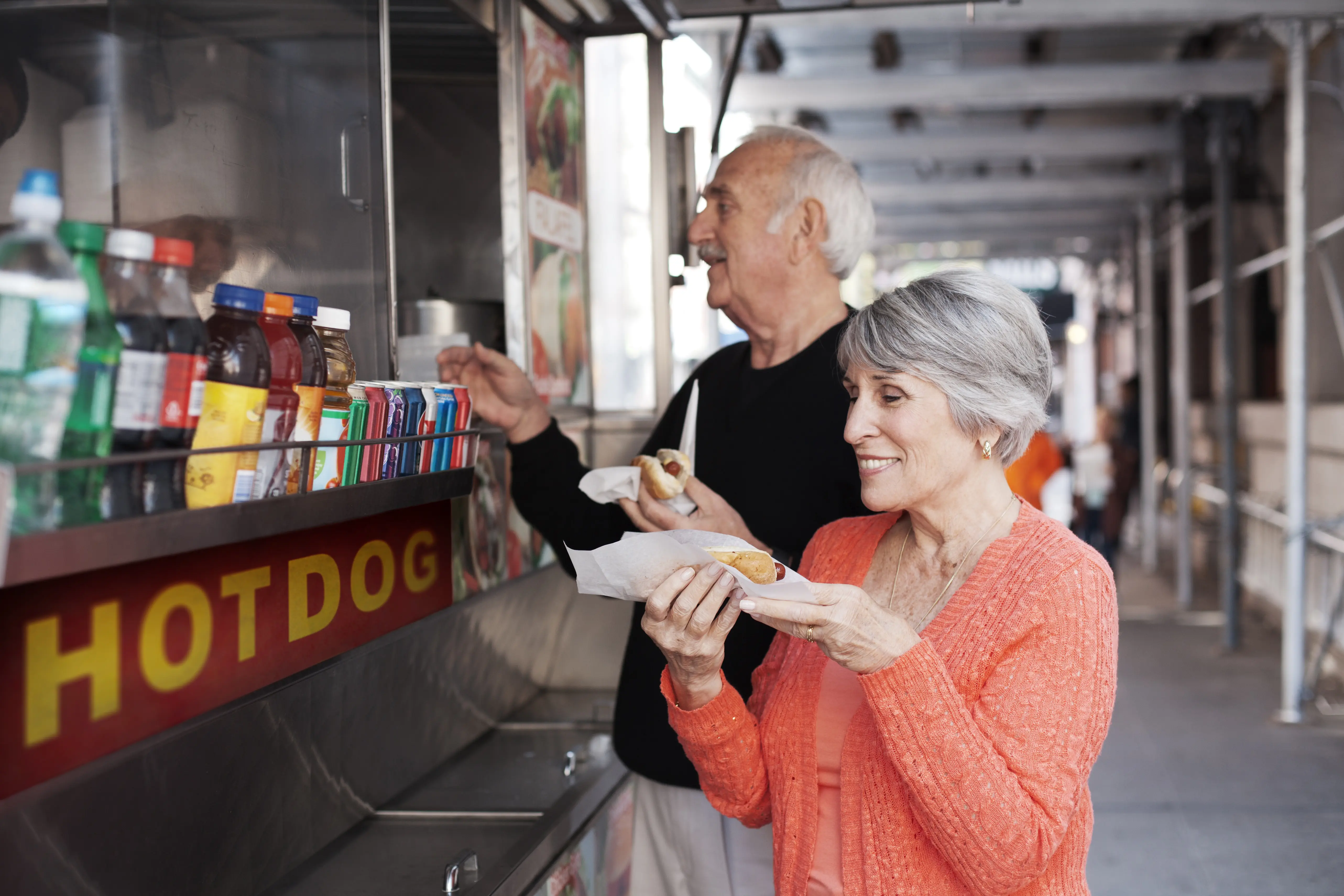 Outdoor shot of a couple getting hot dogs from a food cart.