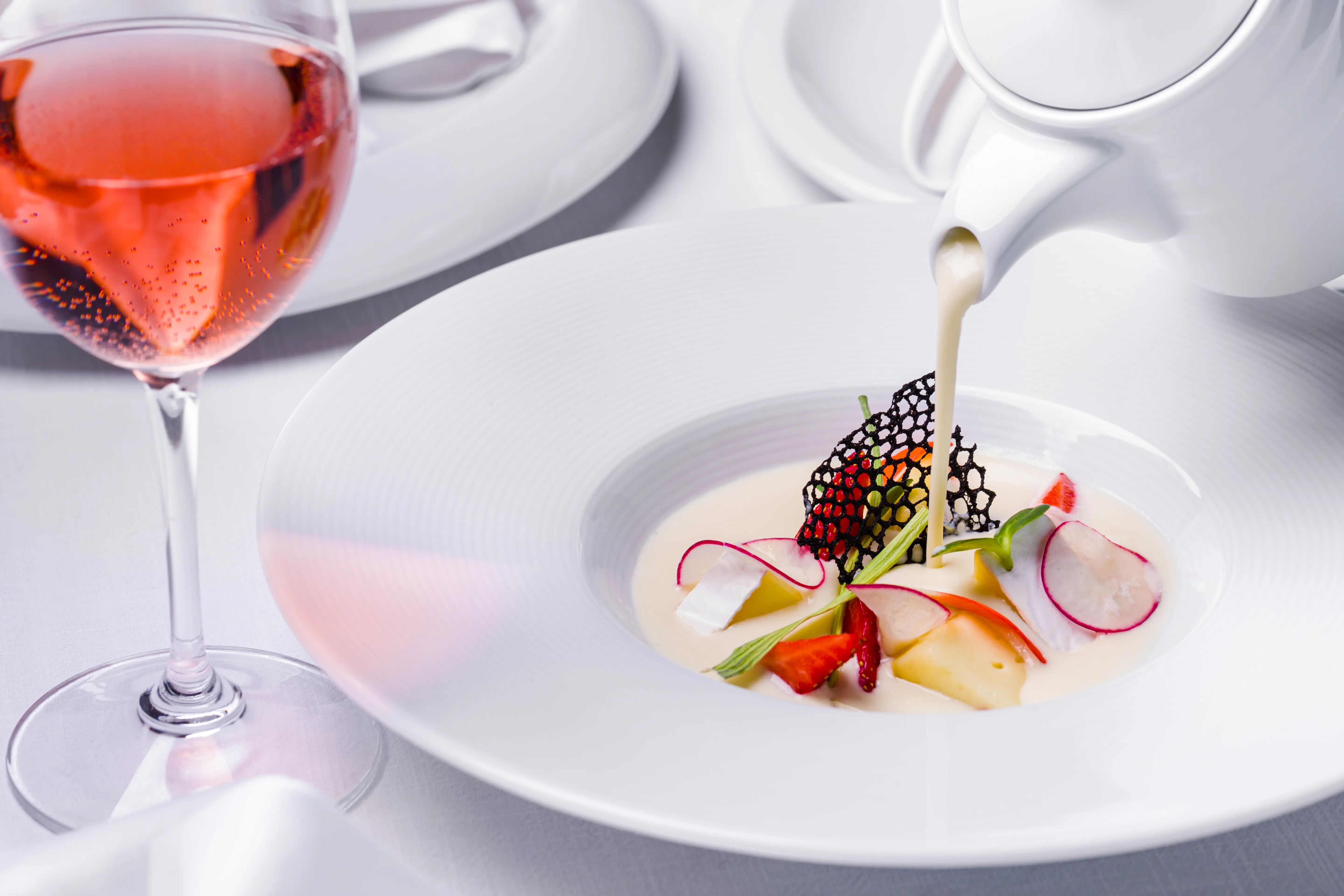 Creamy soup poured onto vegetables in a white wide rim bowl with a glass of rosé