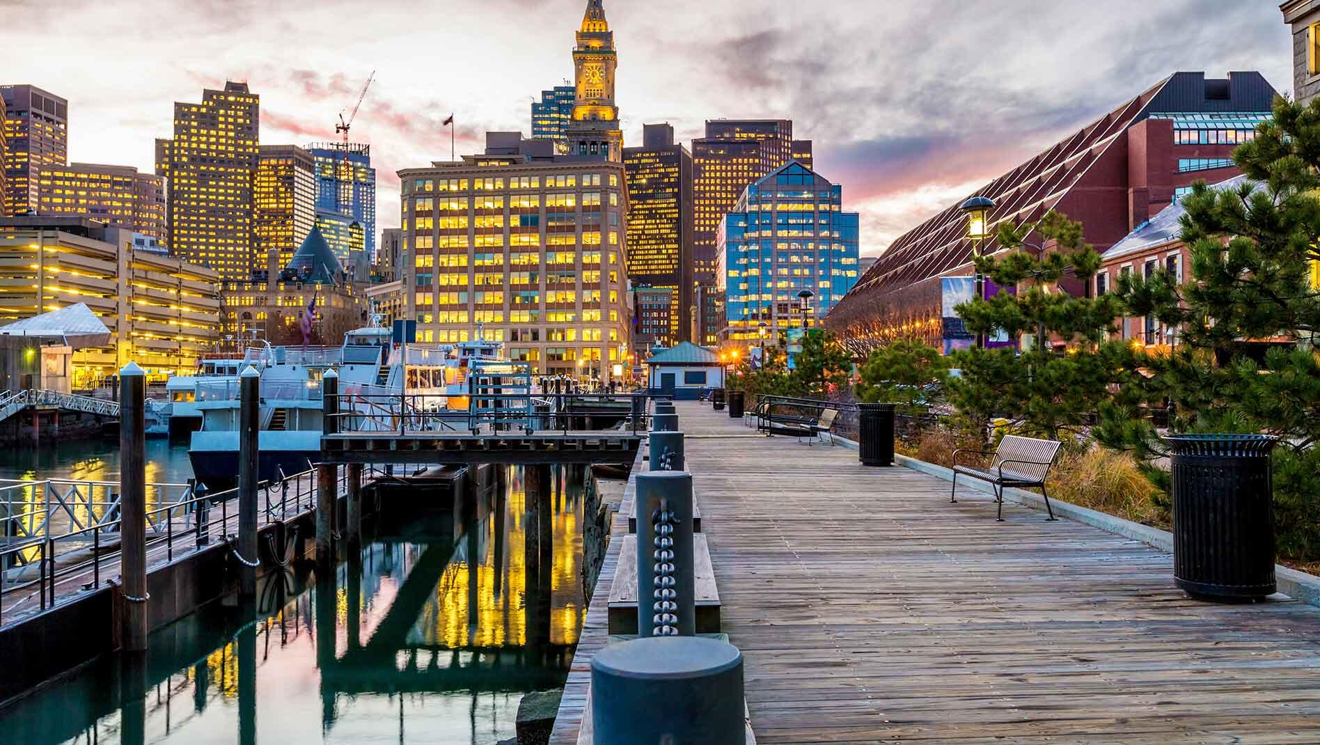 The pier at the Boston Seaport with a view of the Boston skyline as the sun sets.