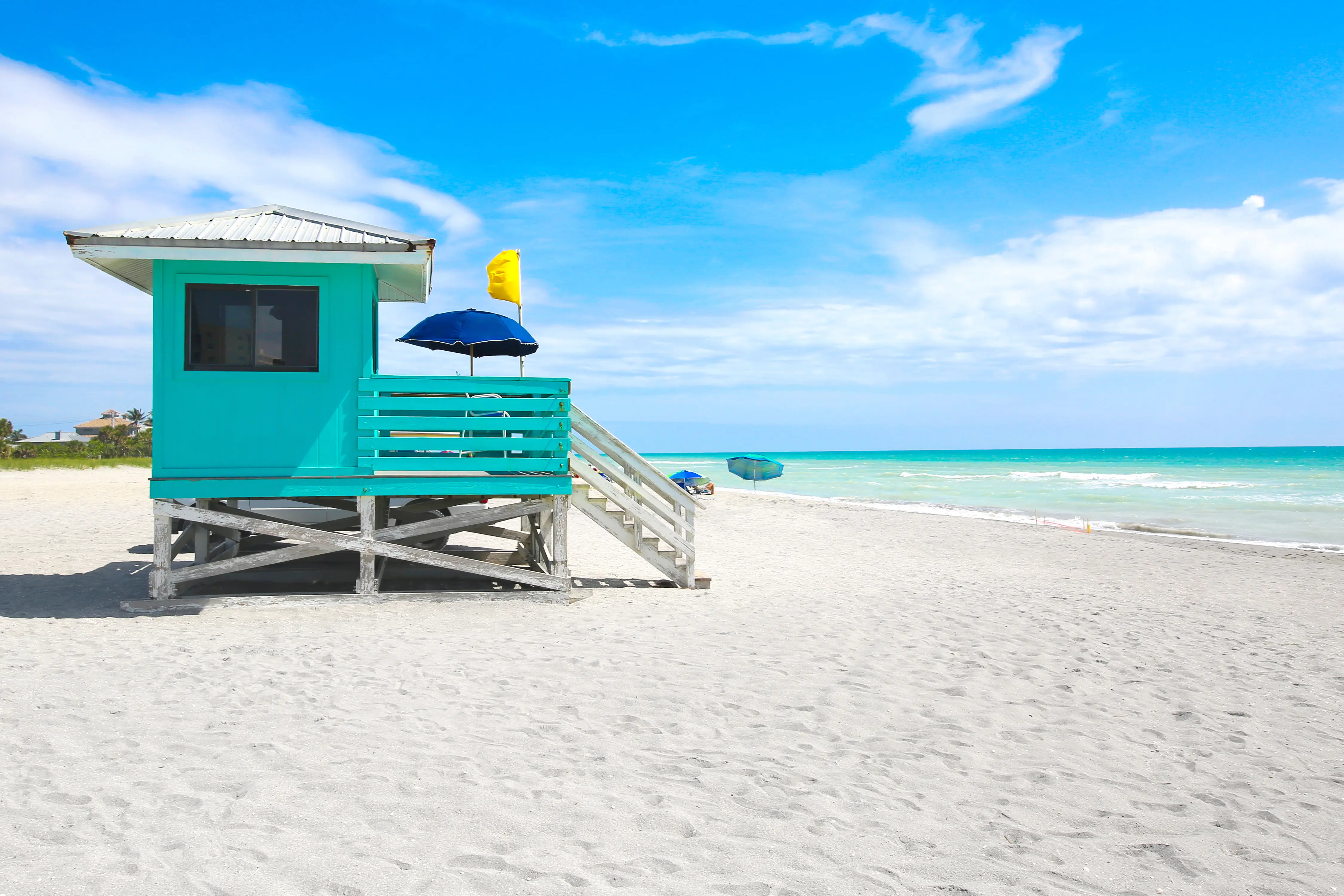 Isolated turquoise lifeguard hut along a white sandy beach and bright blue ocean
