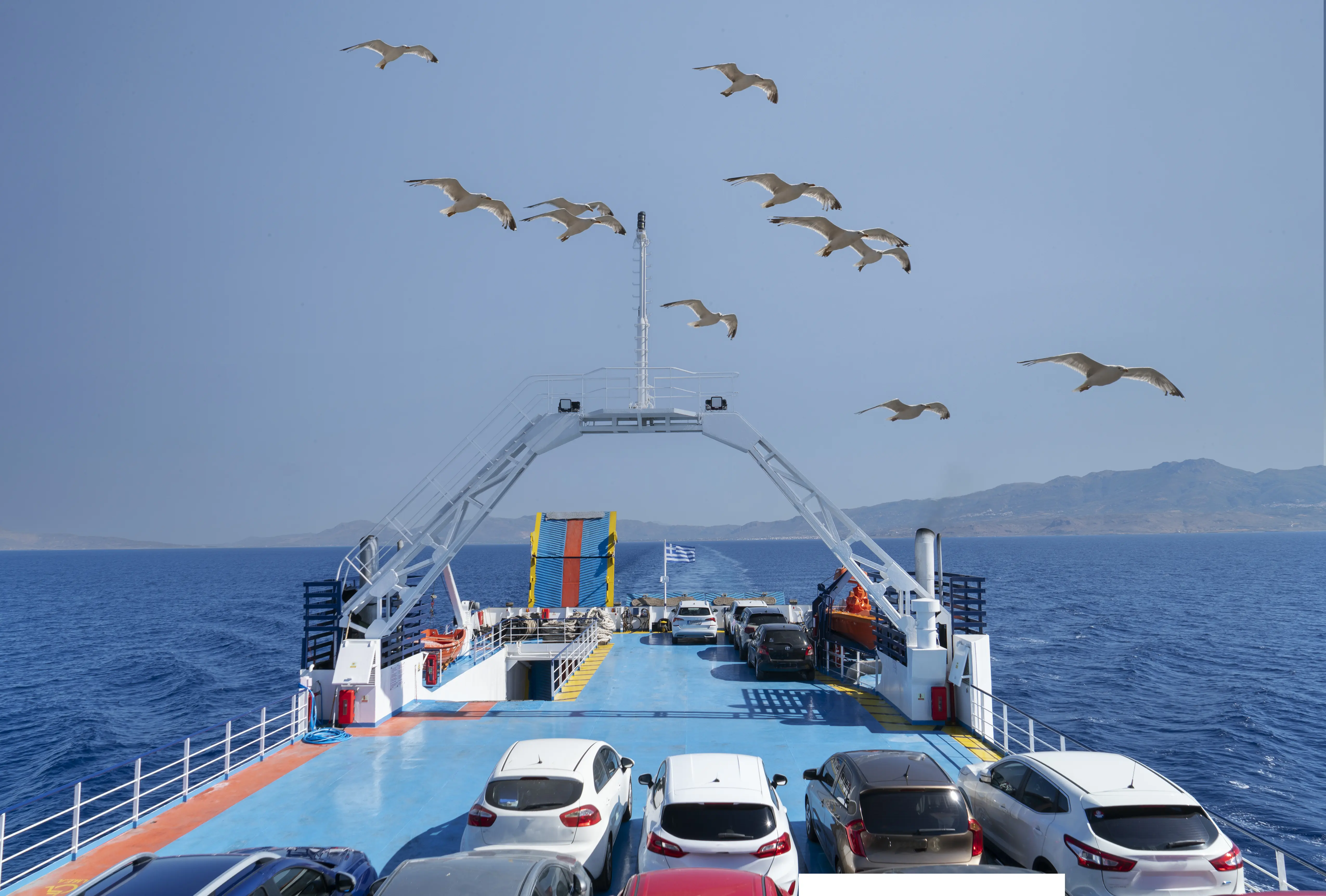 Image of a ferry boat in Greece transporting cars and people, with seagulls flying overhead.