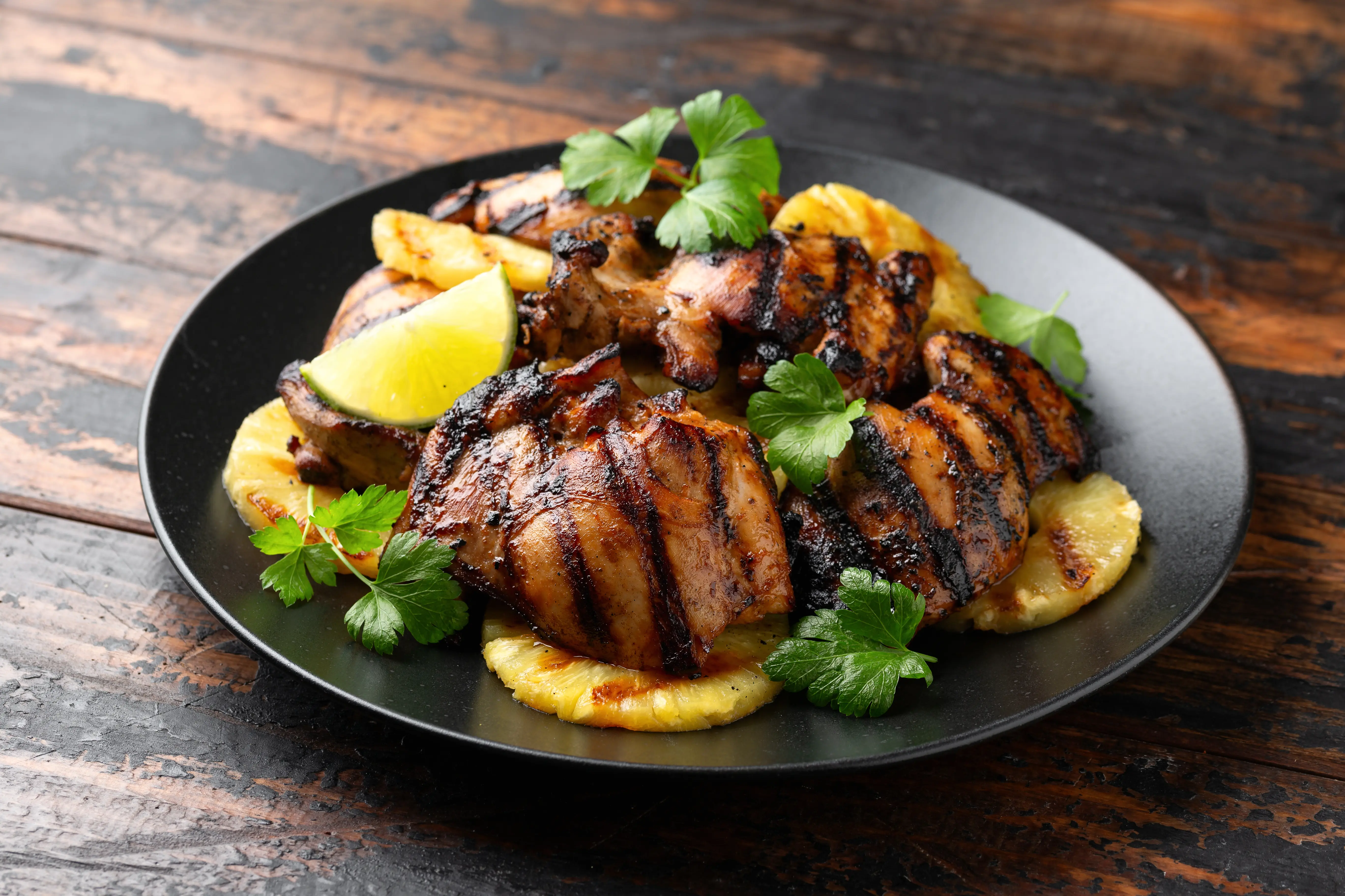 Hawaiian Huli Huli Chicken with pineapple served on black plate ontop of wooden table
